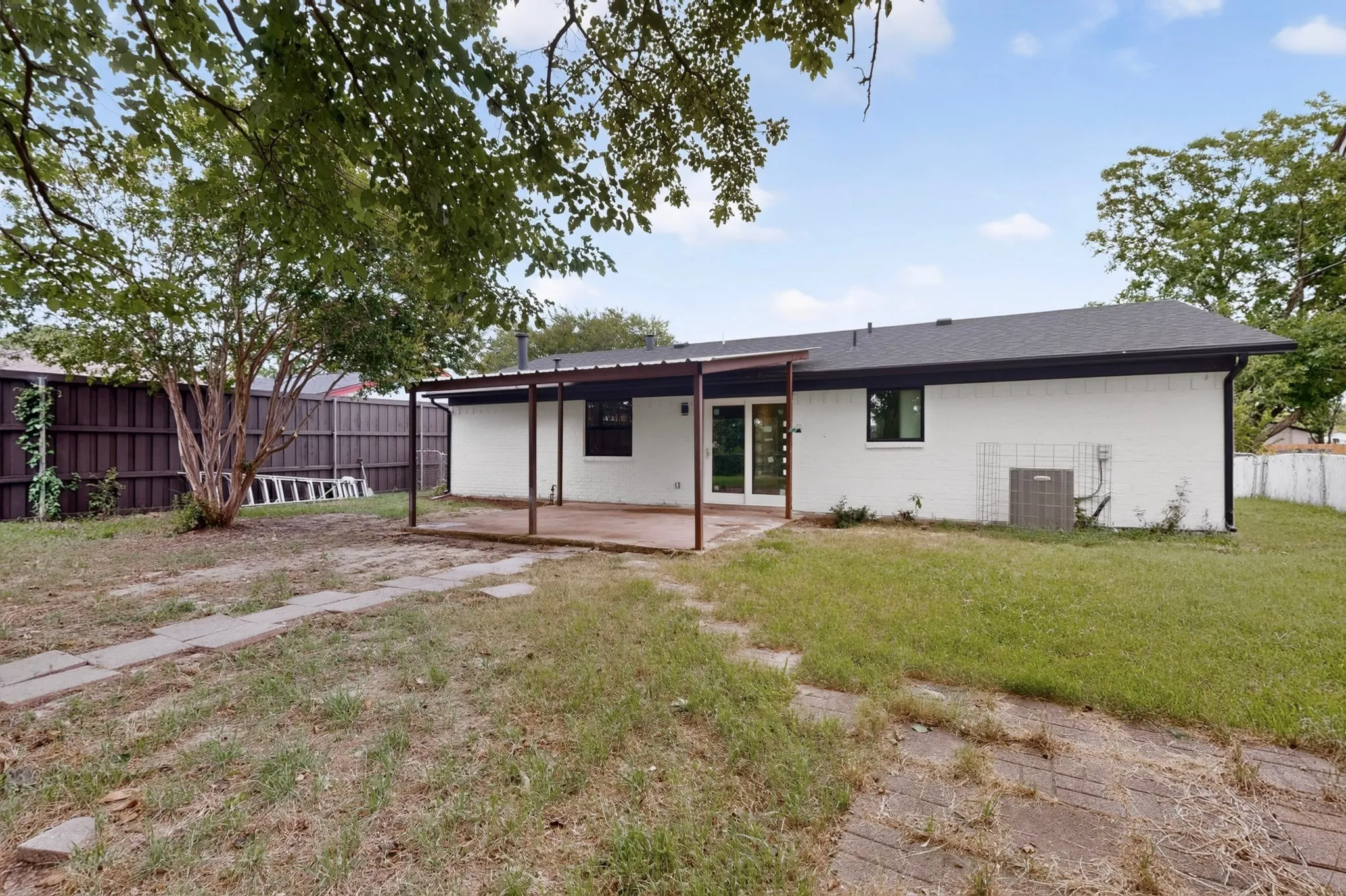 Rear exterior featuring white brick siding and a black shingle roof
