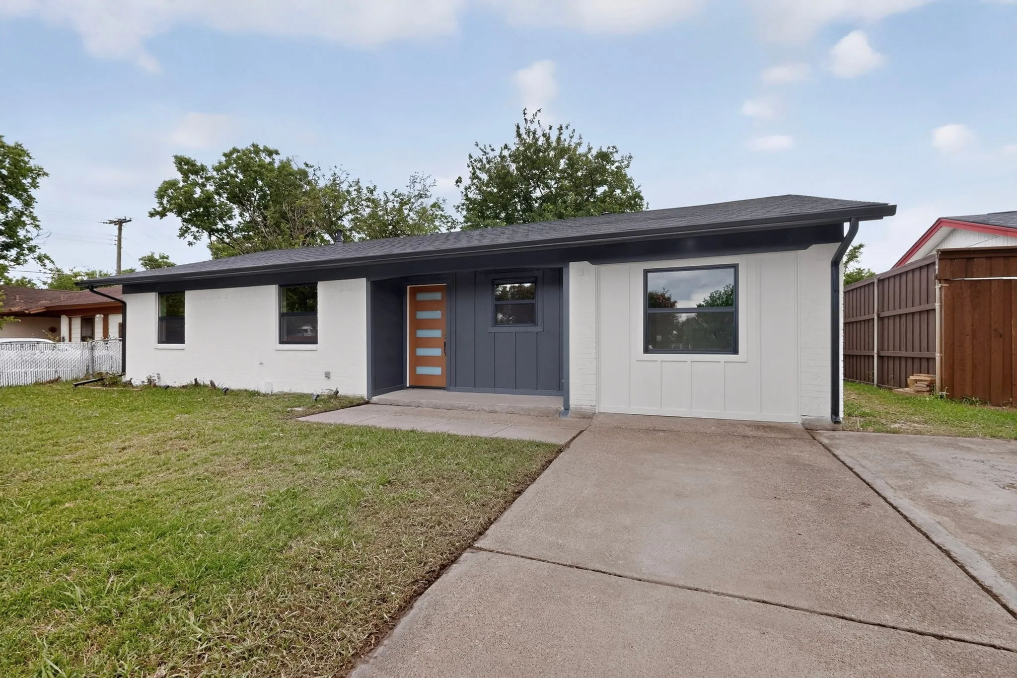 Modern exterior featuring a light wood-finish front door, white painted brick, charcoal gray siding, and a dark roof