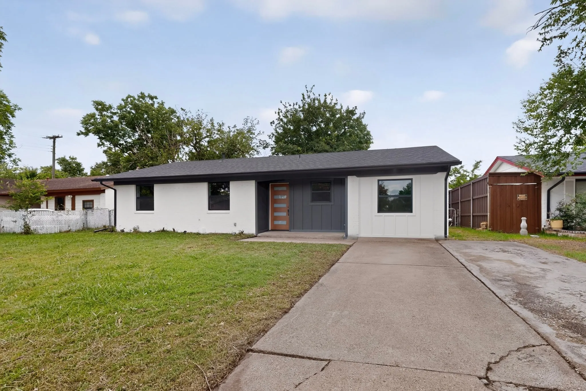 Exterior featuring a dark shingle roof, white and charcoal facade, single-pane windows, and a modern wood-finish front door with frosted glass inserts