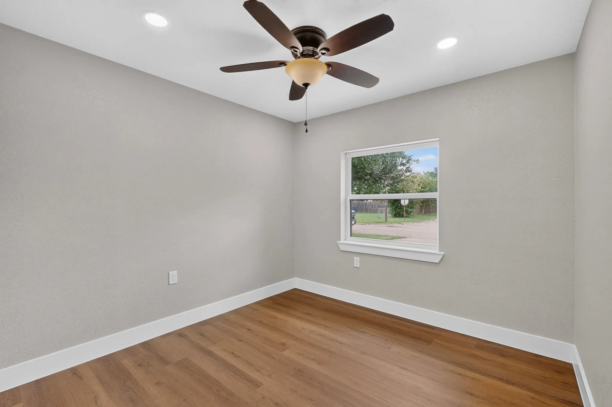 Room featuring wood-finish flooring, light grey walls, white baseboards, and a single window with white trim