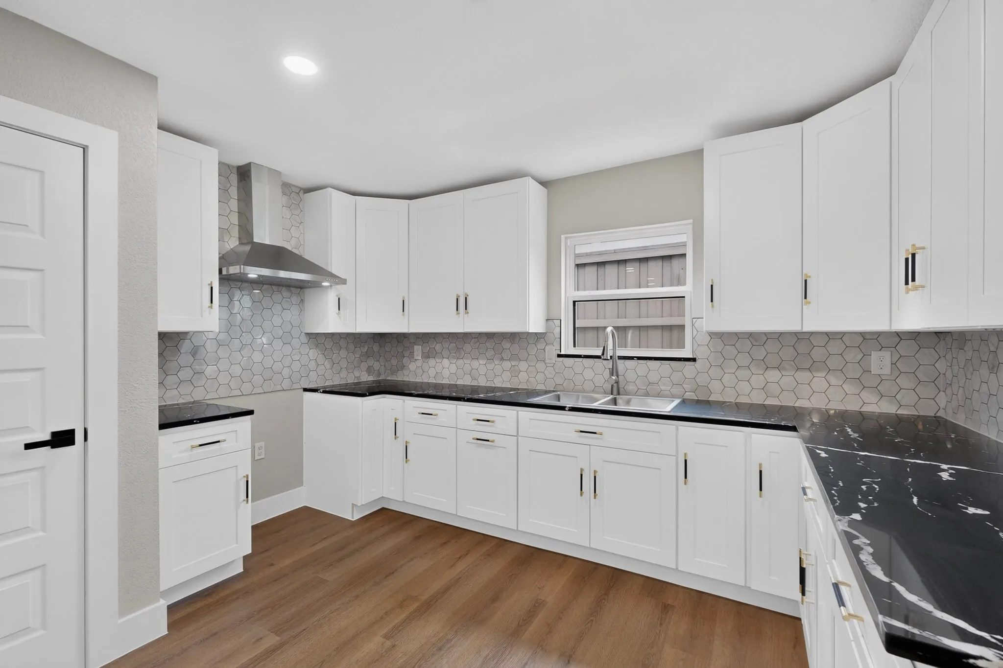 Modern kitchen featuring white cabinetry, dark countertops, a mosaic tile backsplash, wood-finish flooring, and a stainless steel range hood
