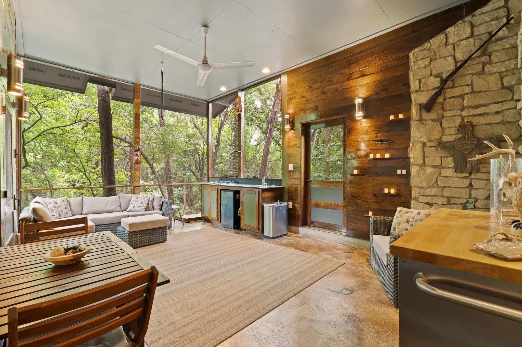 Expansive, yet cozy screened-in porch featuring a wood-finish accent wall and outdoor kitchen. Two doors leading outside.
