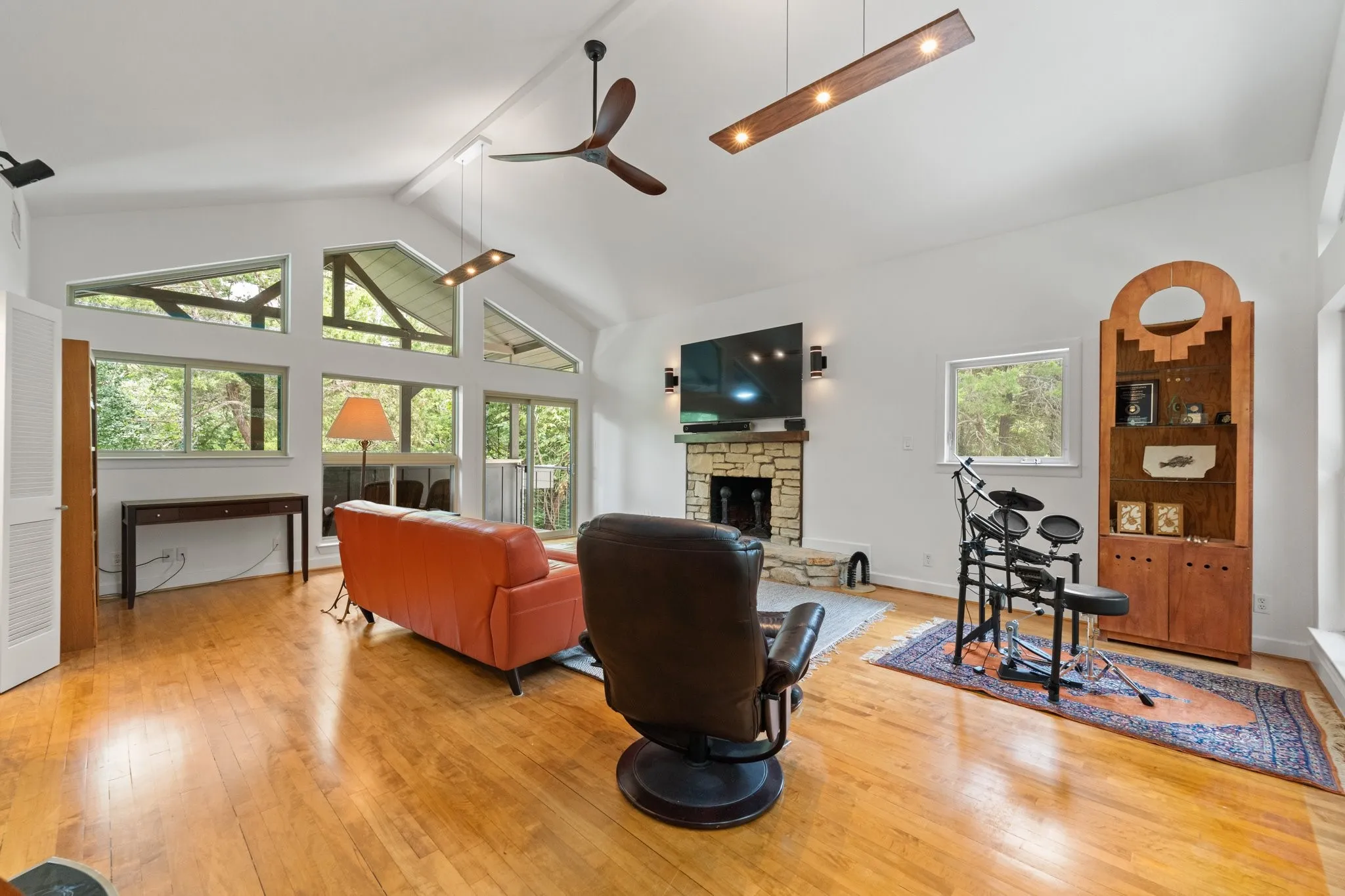 Spacious upstairs living area featuring a vaulted ceiling with exposed beams, wood-finish flooring, a stacked stone fireplace, and ample natural light from multiple windows - the views are unbelievable - you have to see it for yourself