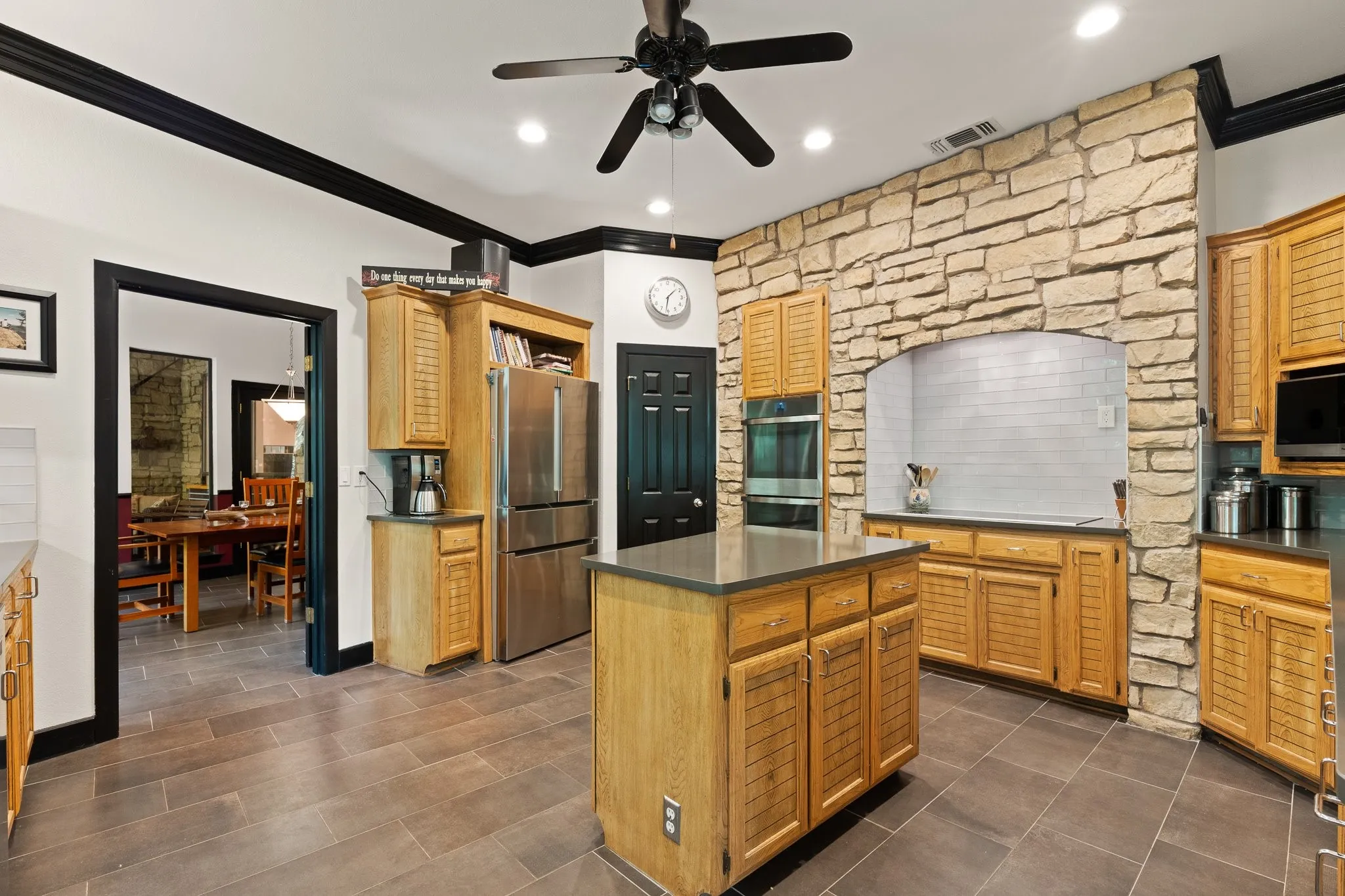 Large Kitchen featuring a stone arch accent wall, cabinets galore, stainless steel appliances, a central island with an abundance countertop space