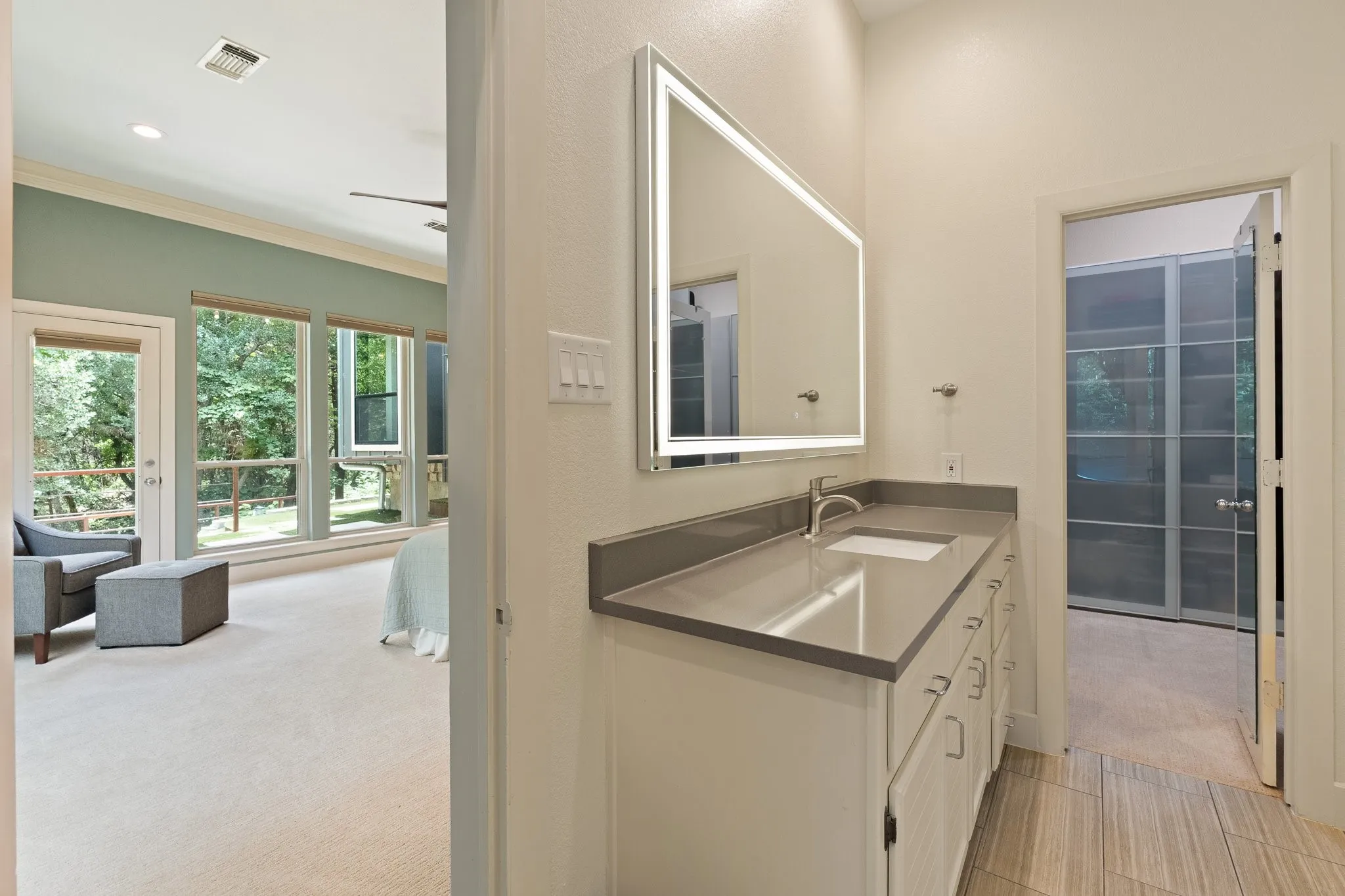 One of two separate countertops and illuminated mirror in the primary bathroom - peeking inside the large custom closet