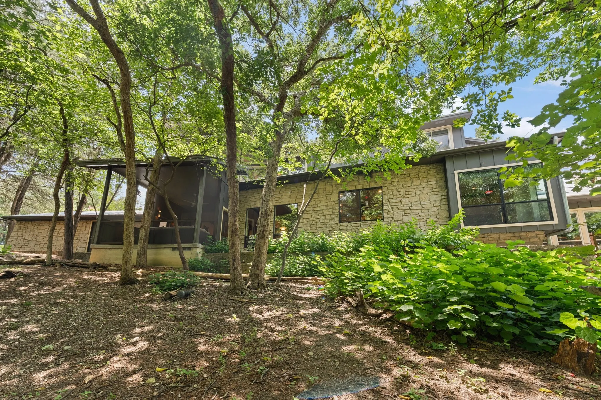 Back of the home featuring large pane windows, the cozy and relaxing screened porch, and mature trees surrounding the property, the landscape is unbelievable and must be experienced in person.