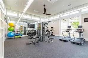 Fitness room featuring gray carpet flooring, a ceiling fan, a wall of mirrors, and large sliding glass doors