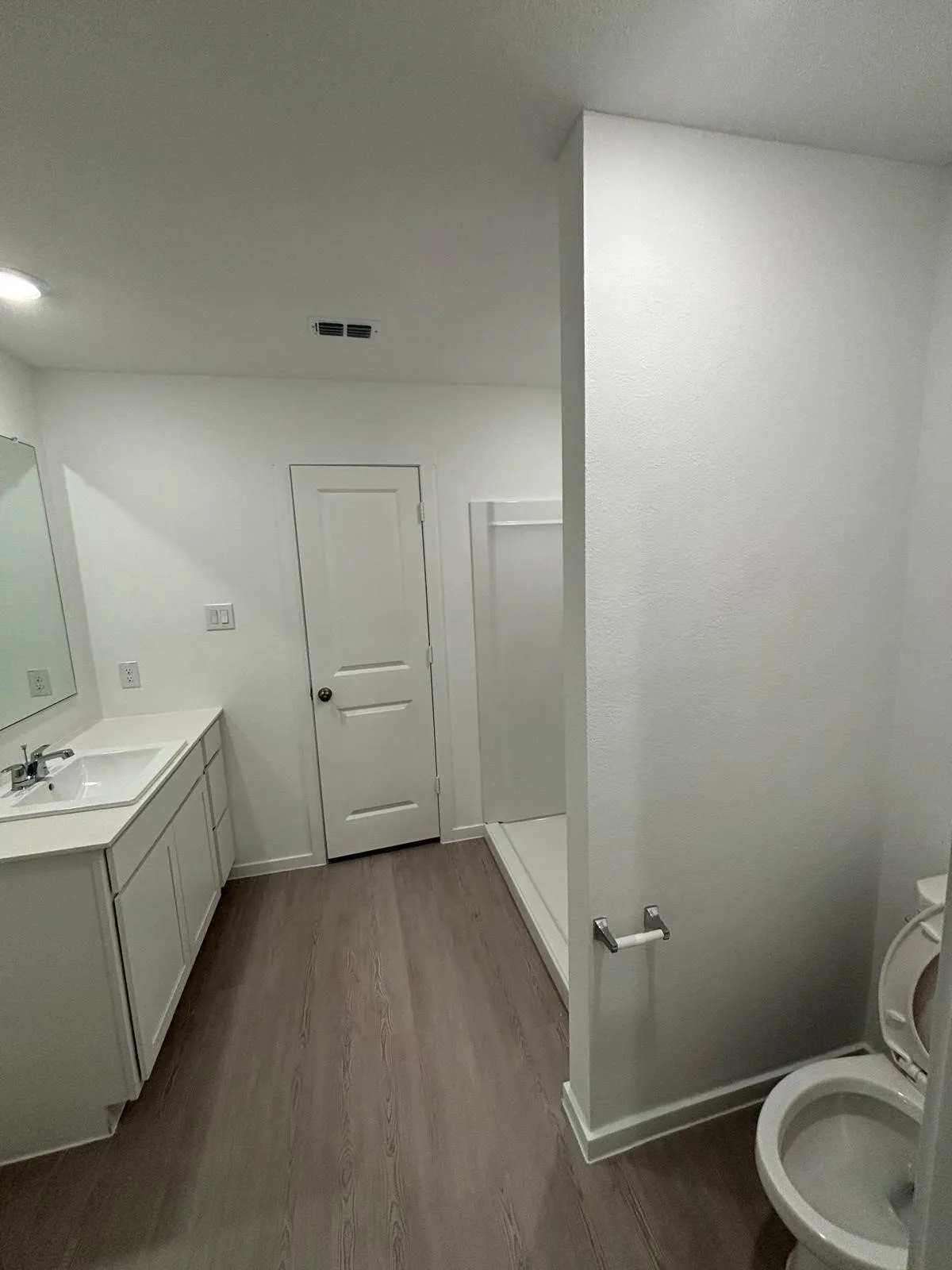 Contemporary bathroom featuring a light wood-finish floor, white vanity with an integrated sink, polished chrome faucet, and a shower stall