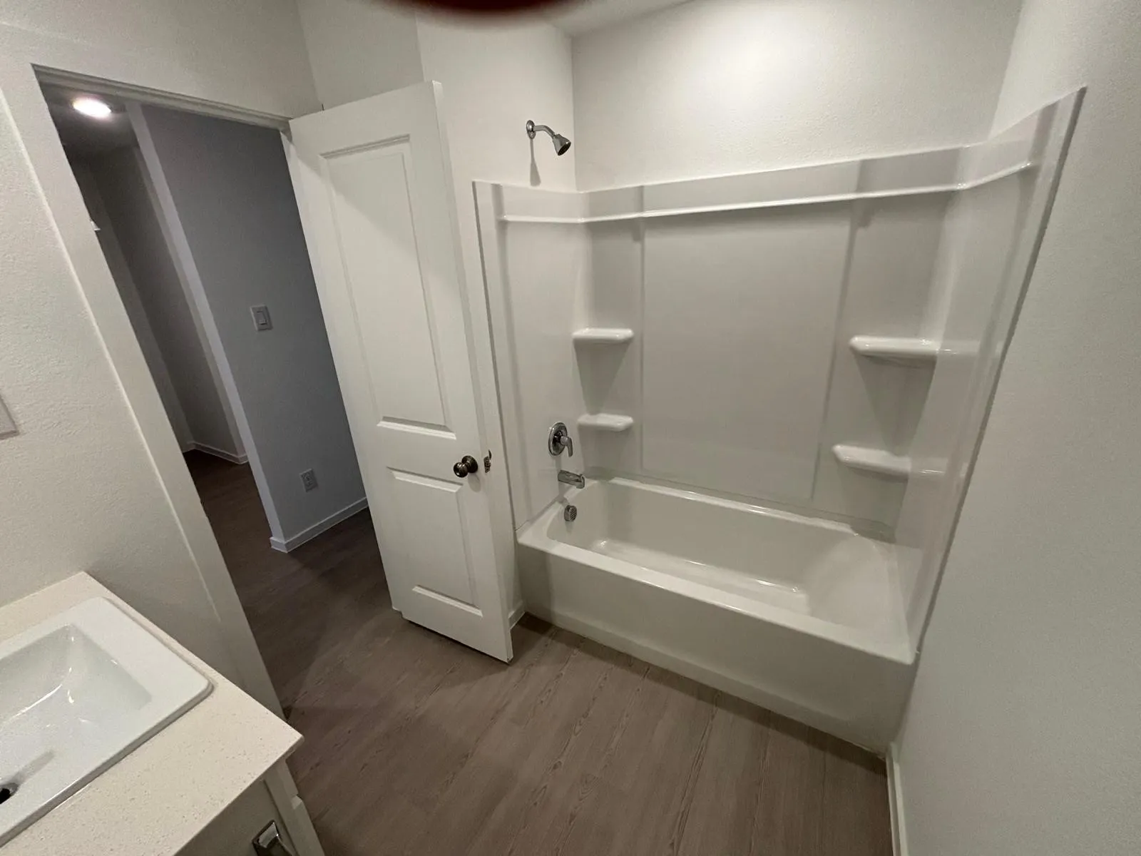 Bathroom featuring a white bathtub with an integrated shower, chrome fixtures, and a light wood-finish floor