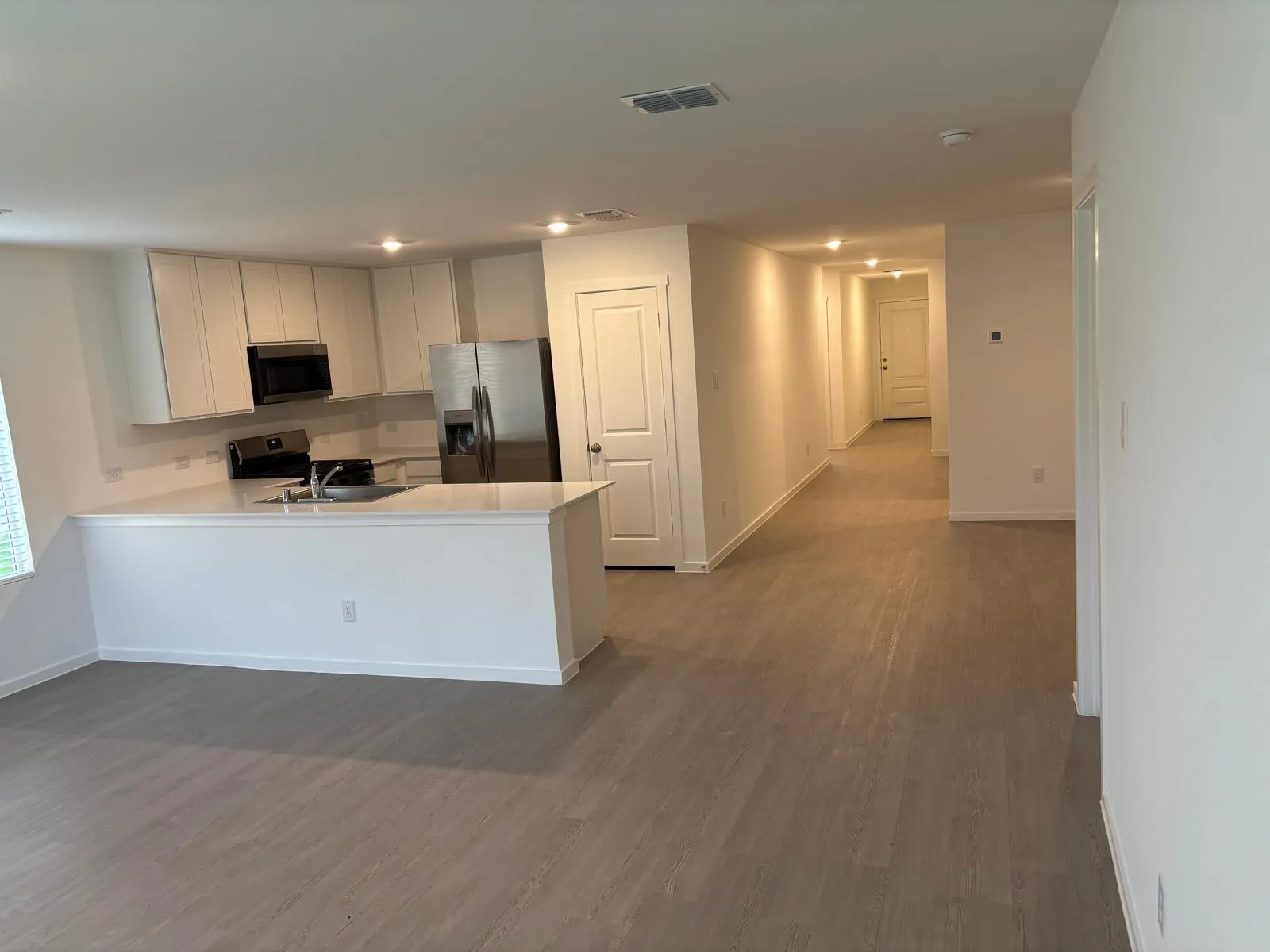 Open-concept living space featuring wood-finish flooring, a kitchen island with sink, white cabinetry, stainless steel appliances, and recessed lighting