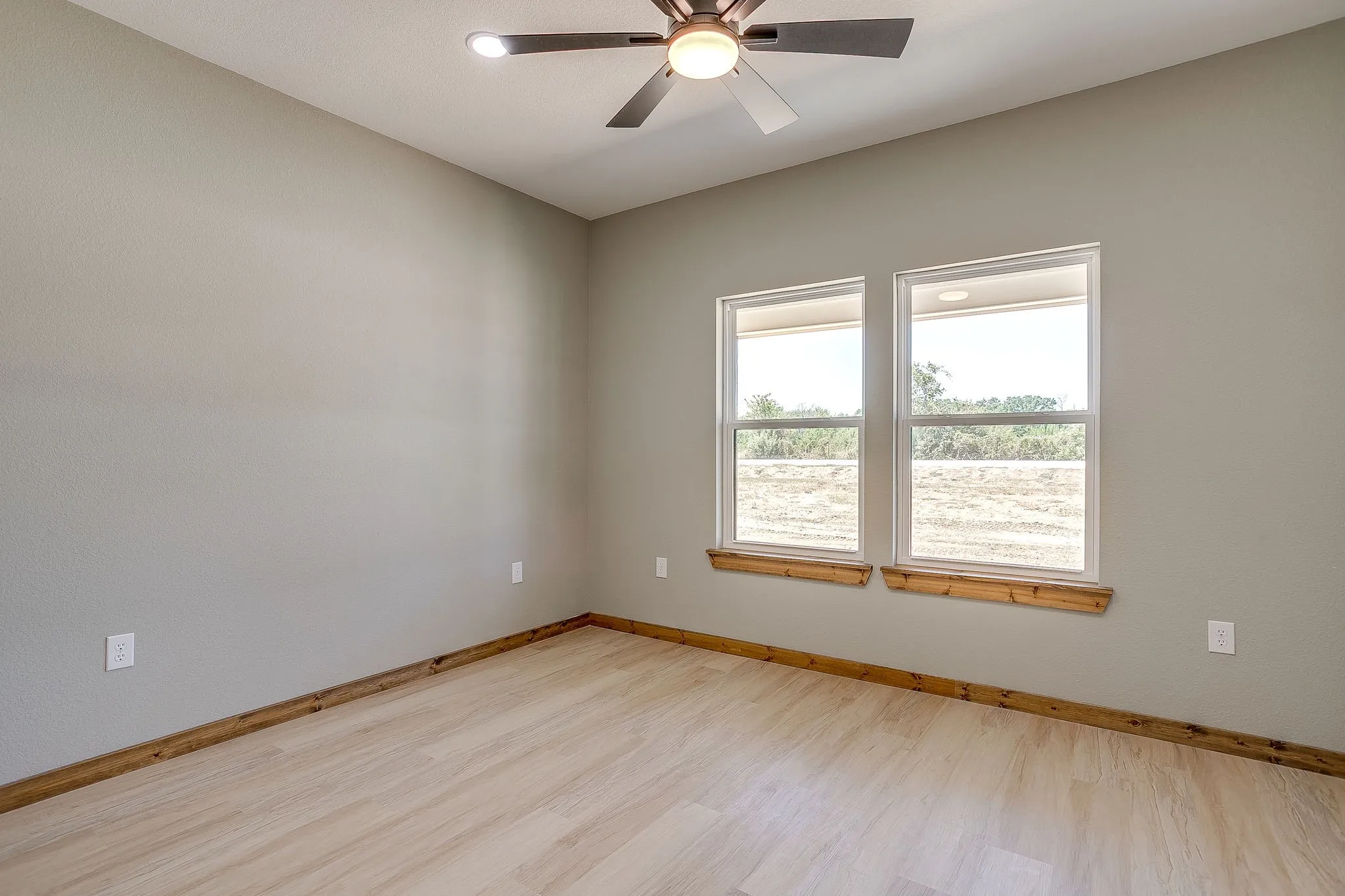 Light-toned wood-finish flooring, two large windows, wood window sills, wood floor trim, and a ceiling fan with integrated lighting