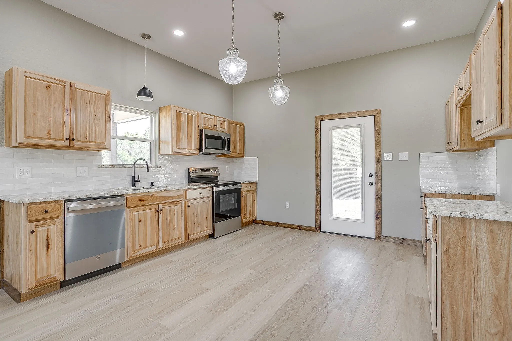 Vaulted ceiling with recessed lighting, light wood-finish flooring, light wood cabinetry, stainless steel appliances, and white subway tile backsplash