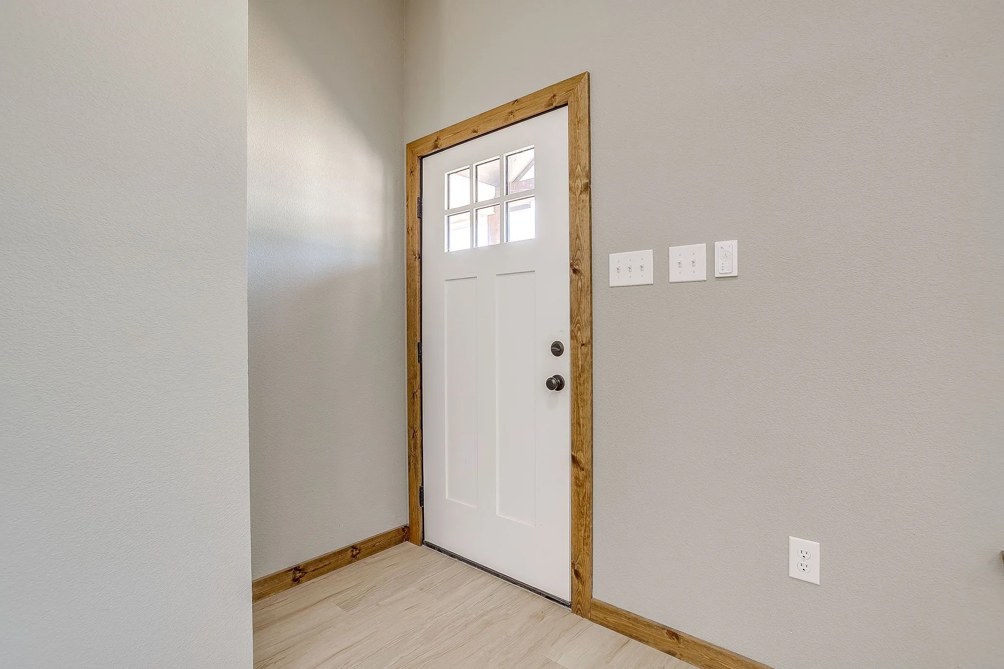 White door with upper window panes, wood-finish trim, and light wood-finish flooring