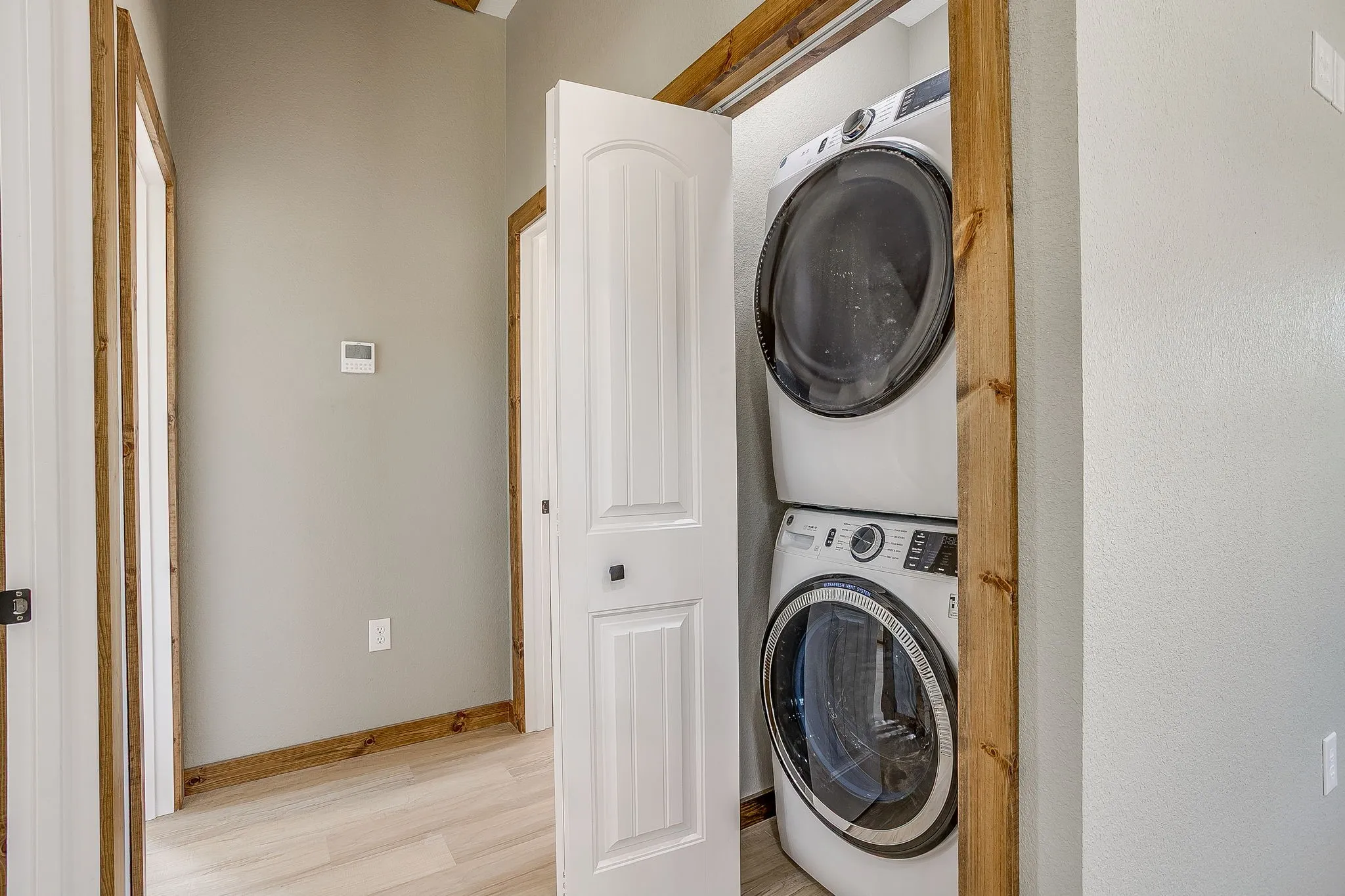 Included Stackable washer and dryer appliances, light wood-finish flooring, white paneled doors, and natural wood trim accents