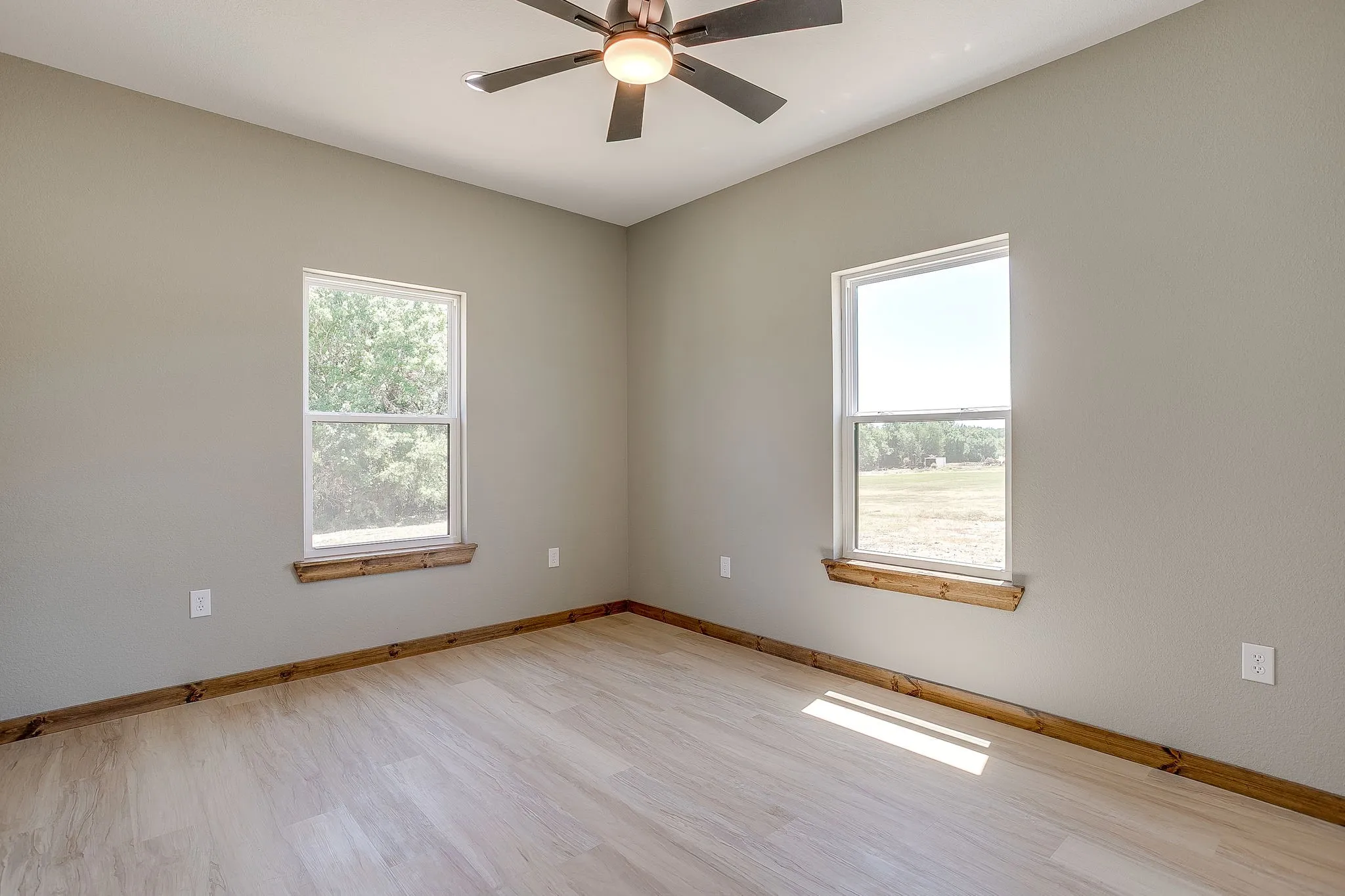 Light wood-finish flooring with wood baseboards, two double-hung windows with wood sills, and a ceiling fan with integrated lighting