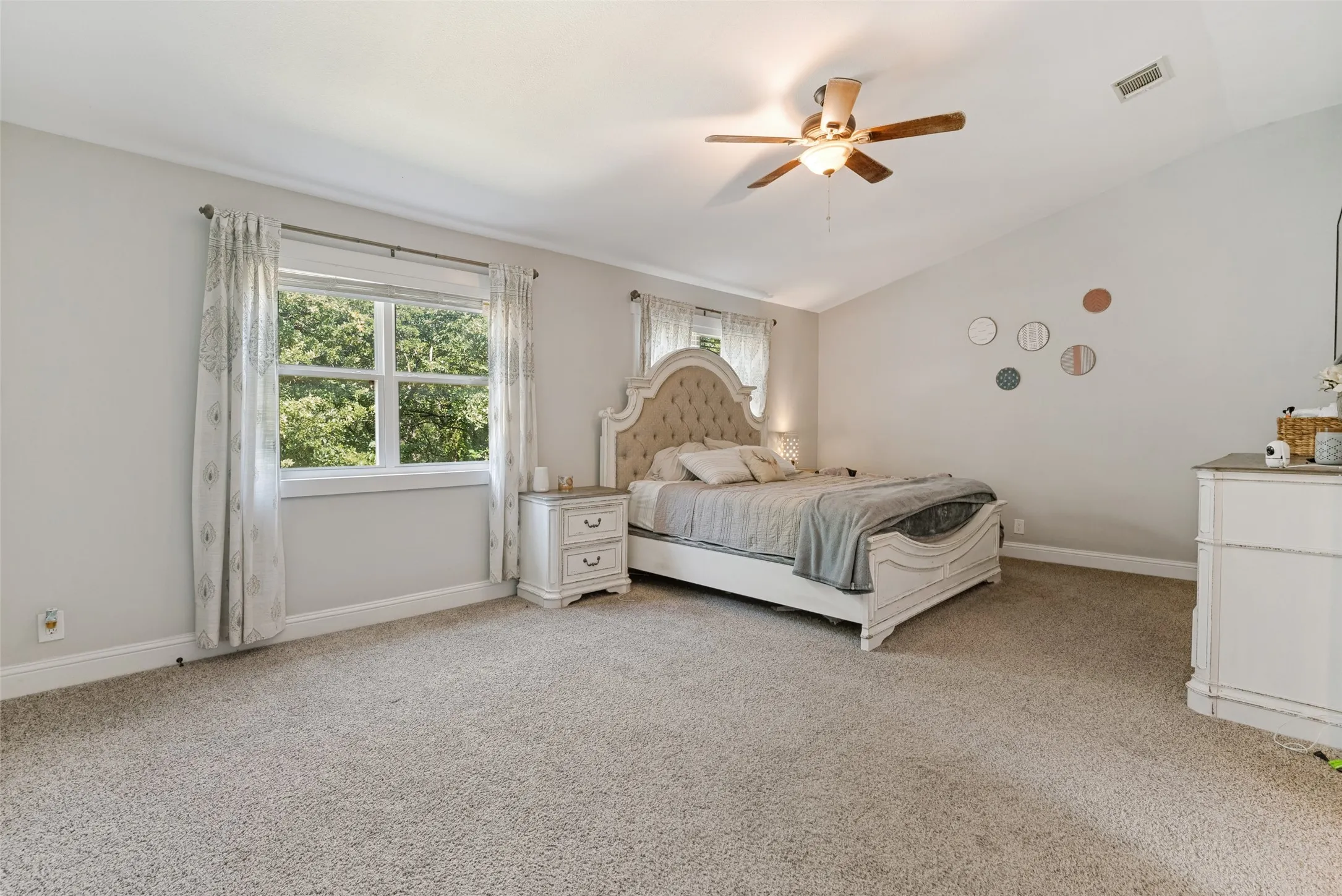Spacious bedroom featuring light-colored carpeting, a vaulted ceiling, and a ceiling fan with light fixture