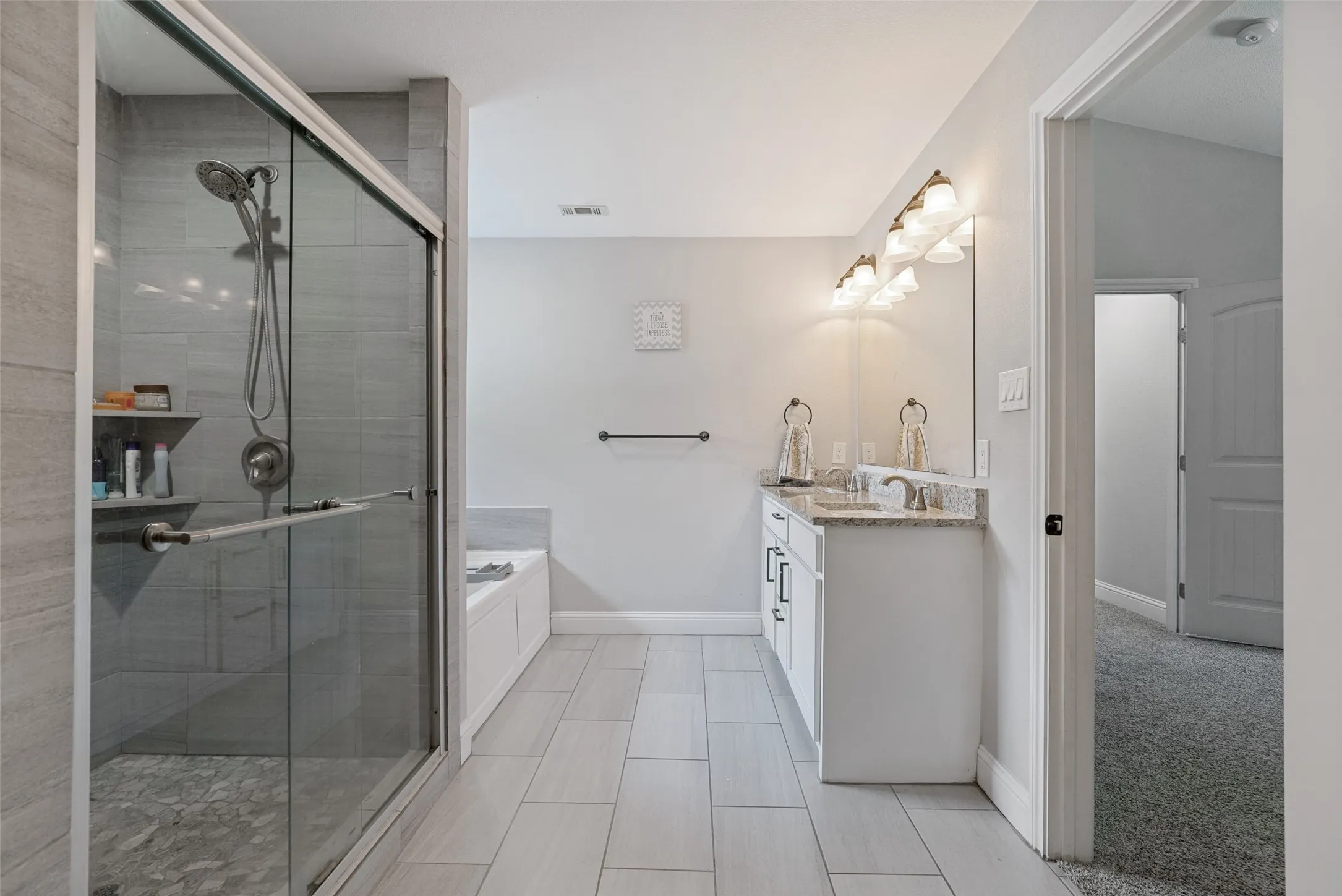 Full bathroom featuring a glass-enclosed shower with tile surround and built-in shelving, a separate soaking tub, and a double vanity with a stone countertop