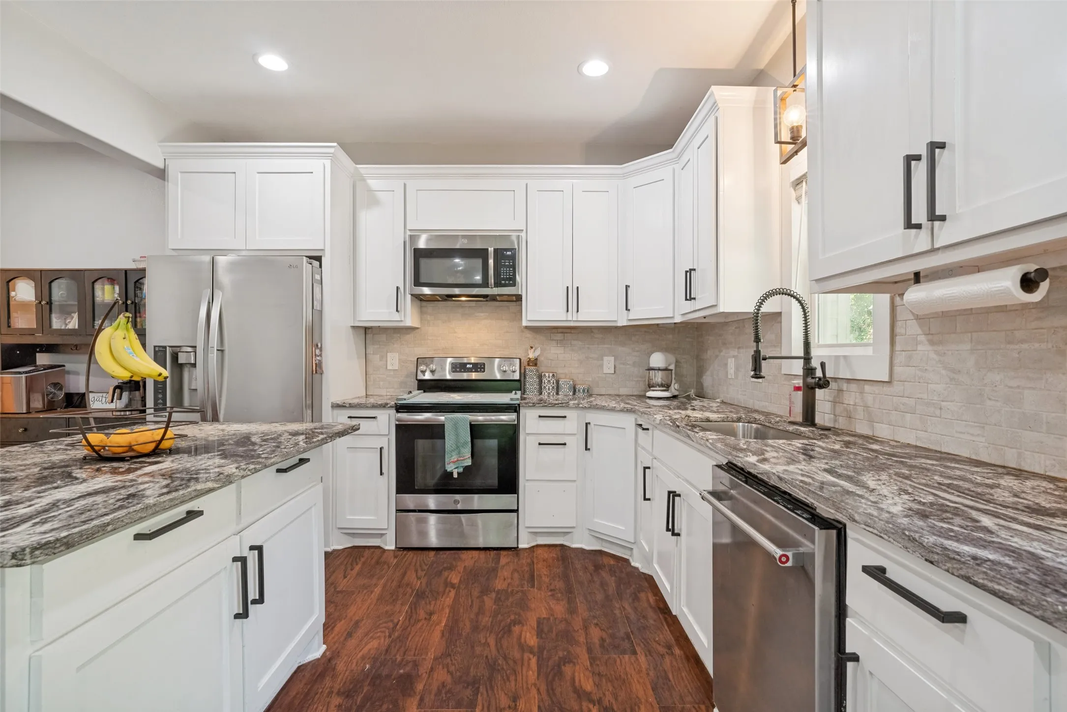 Kitchen featuring white cabinetry with black hardware, stainless steel appliances, dark wood-finish flooring, and light-toned backsplash