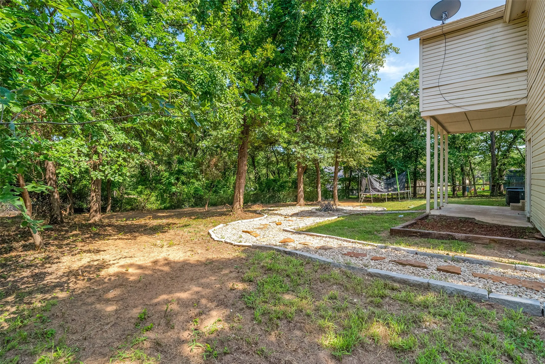 Expansive backyard featuring mature trees, a defined stone pathway, and a covered patio area