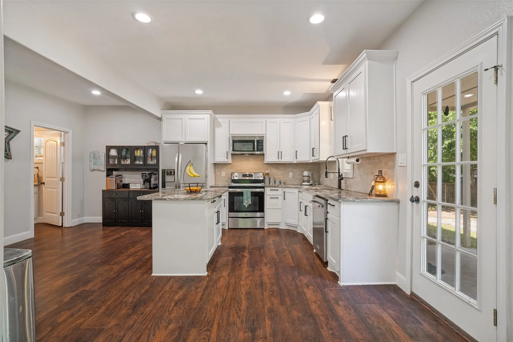 Open-concept kitchen featuring white cabinetry, stainless steel appliances, and a central island with countertop seating