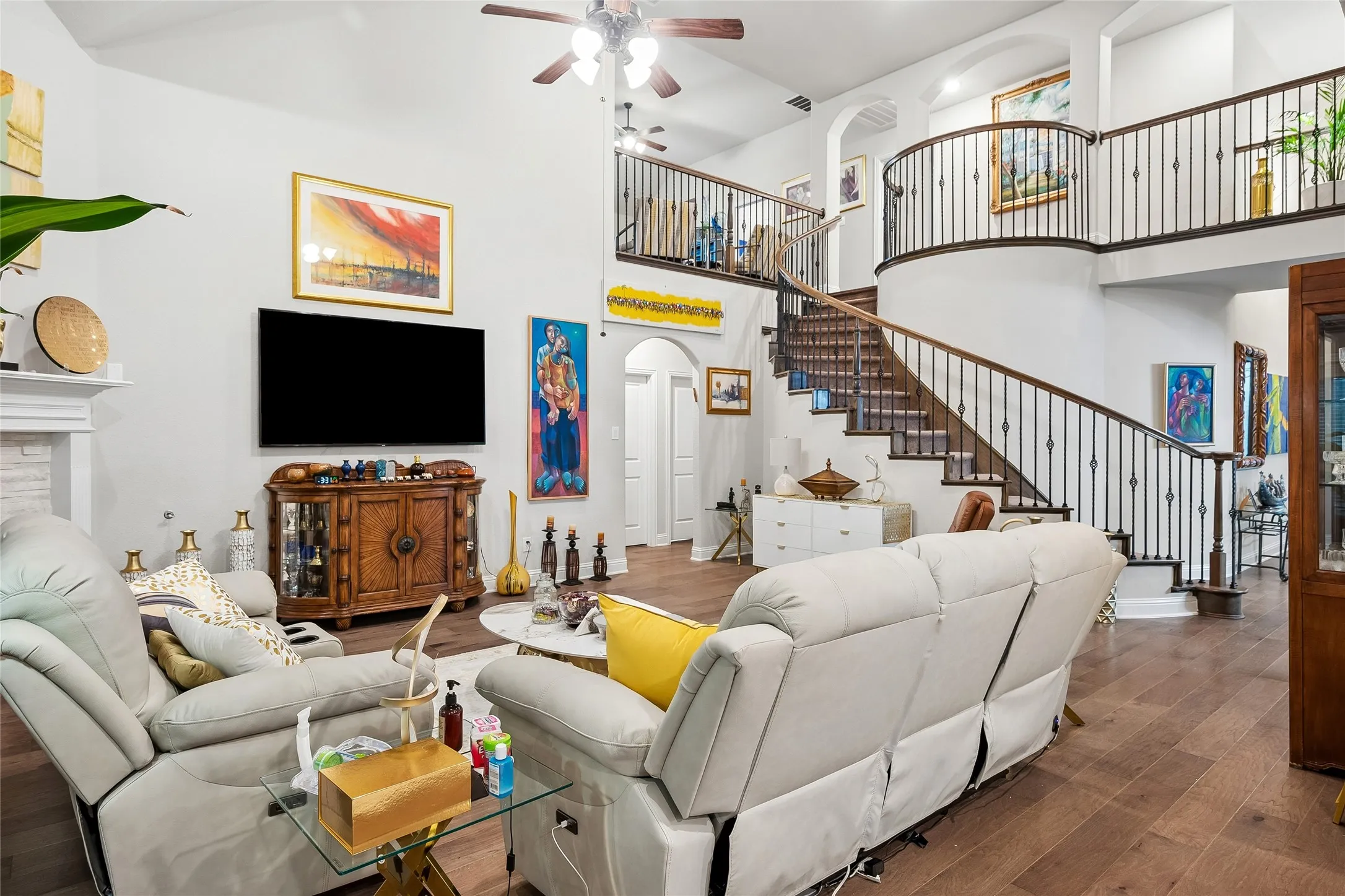 Two story living room with ceiling fan, curved stairs and Juliett balcony
