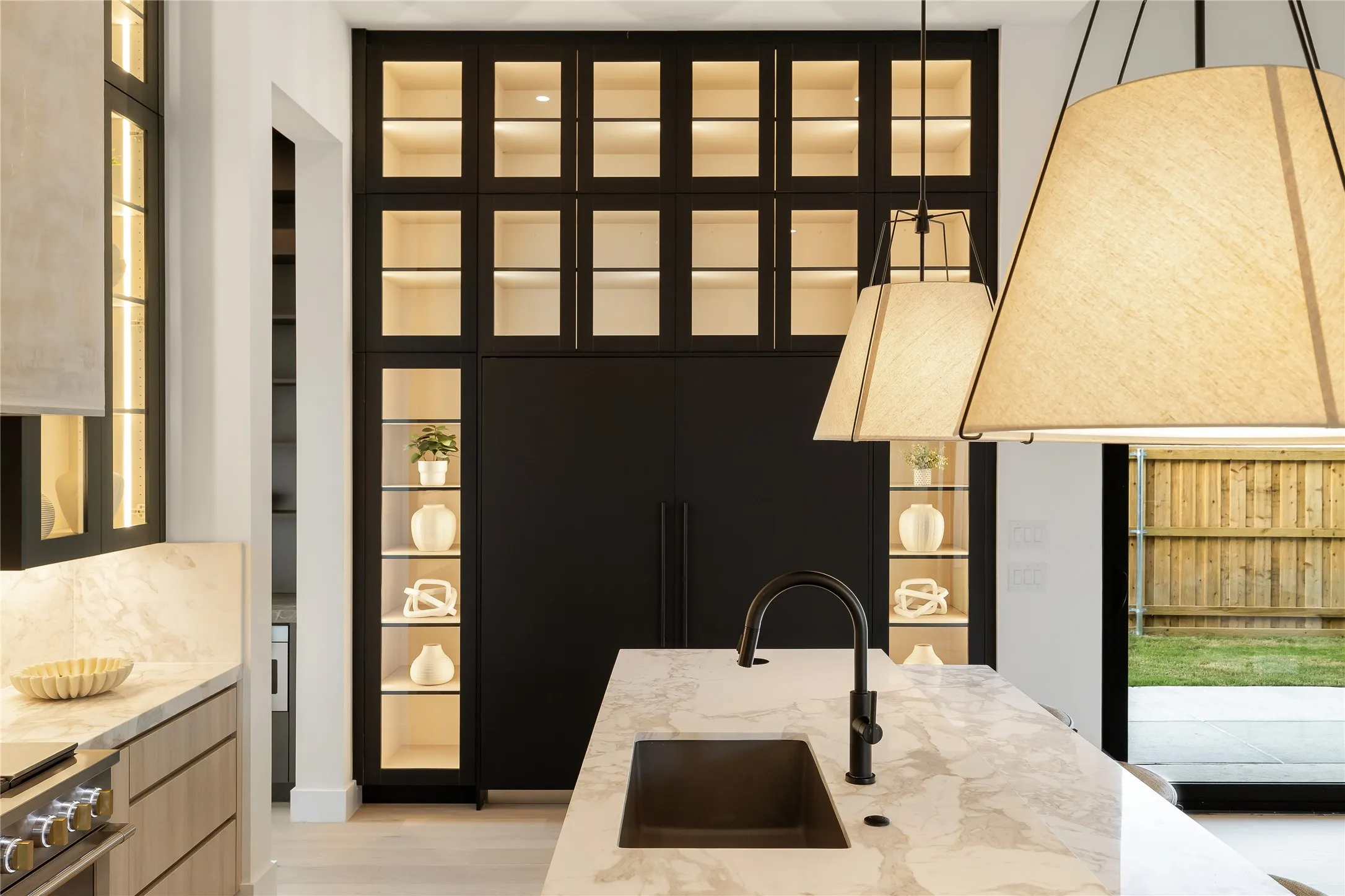 Gourmet kitchen featuring a large island with a dark basin sink and matte black faucet, integrated black paneled refrigerator, back-lit display cabinetry, and light wood-finish lower cabinetry