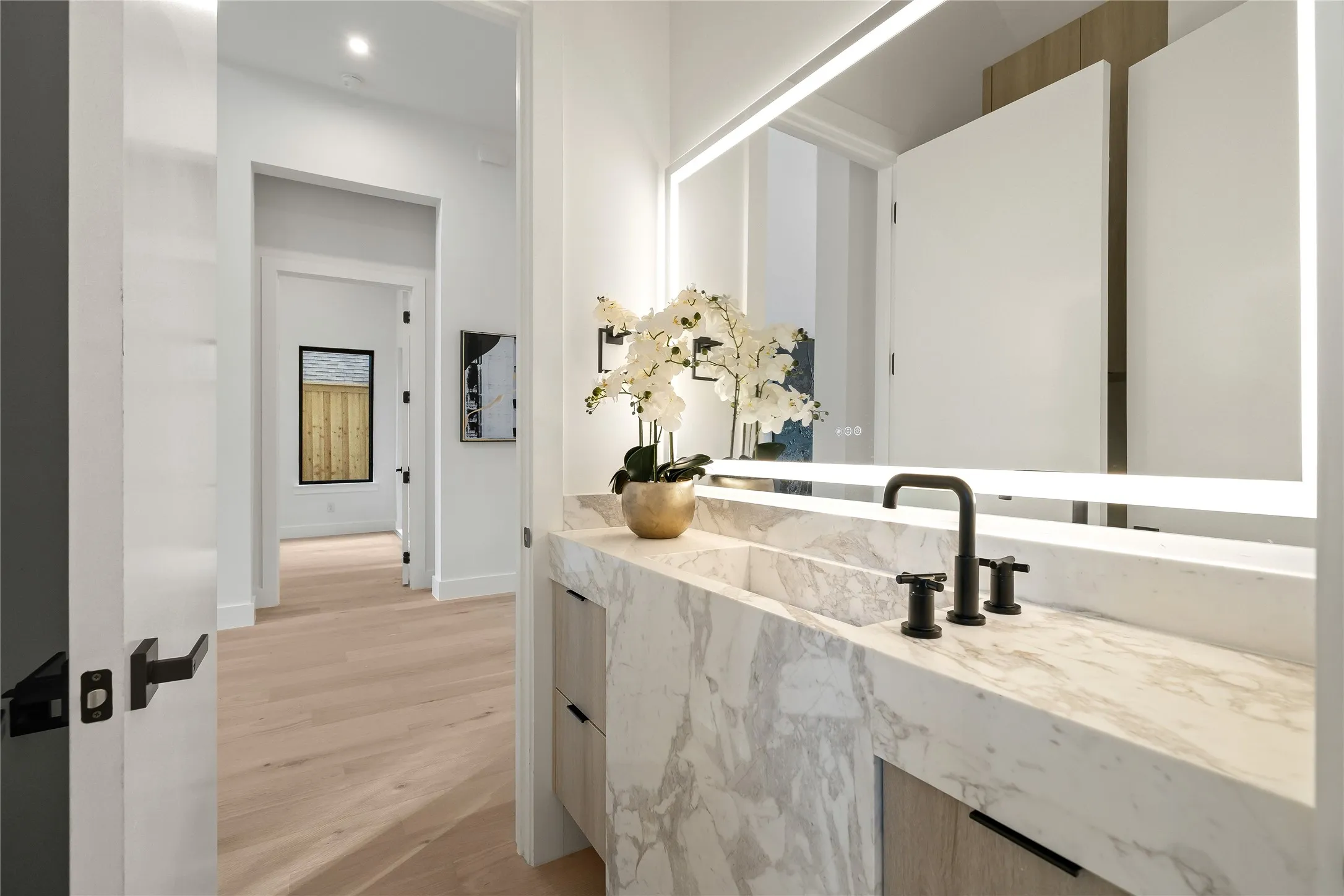 Integrated marble vanity with an undermount sink, matte black three-piece faucet, and a large illuminated mirror