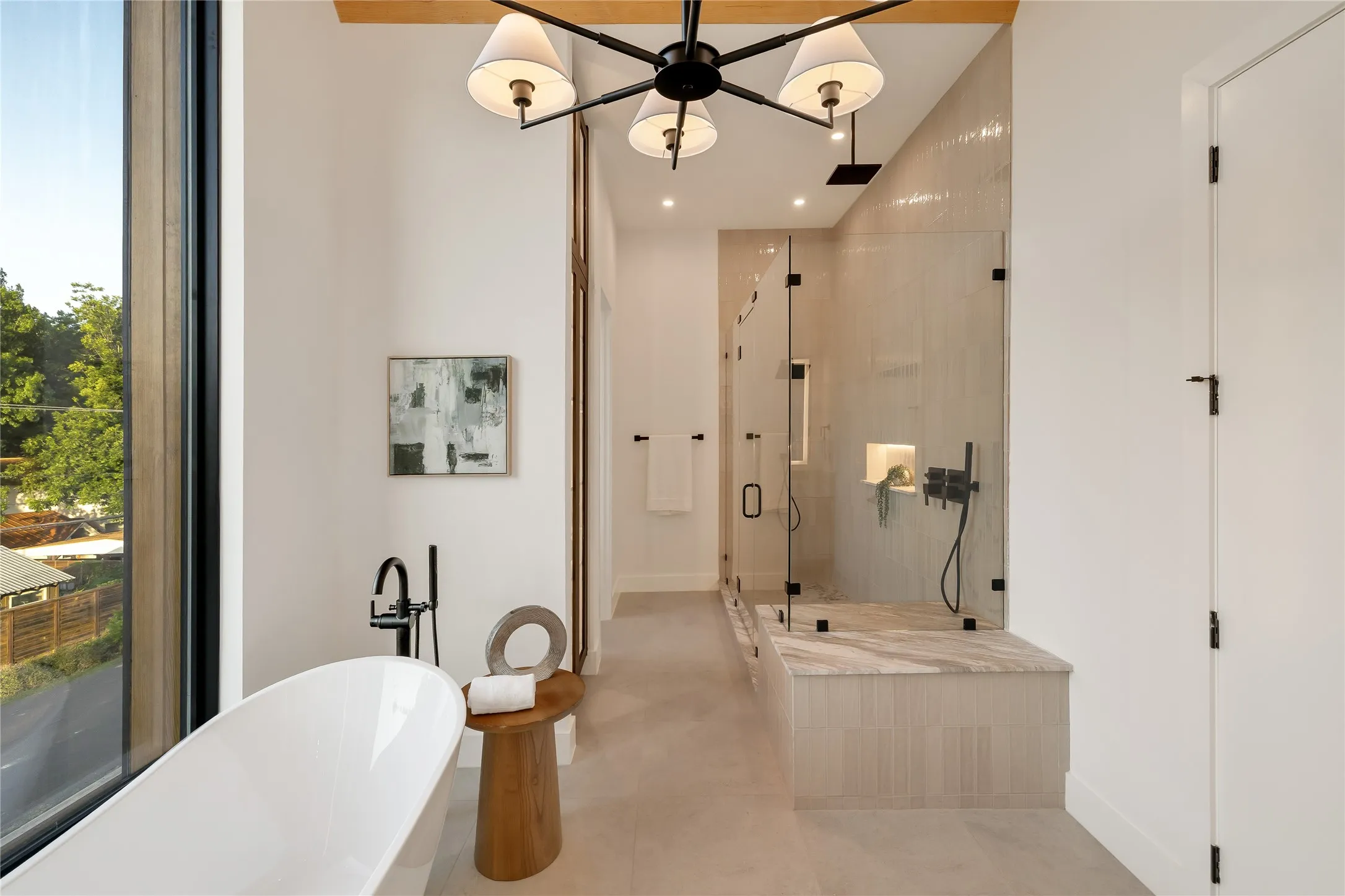 Spacious bathroom featuring a freestanding soaking tub, a large glass-enclosed shower with a built-in bench, contemporary matte black fixtures, and a prominent window