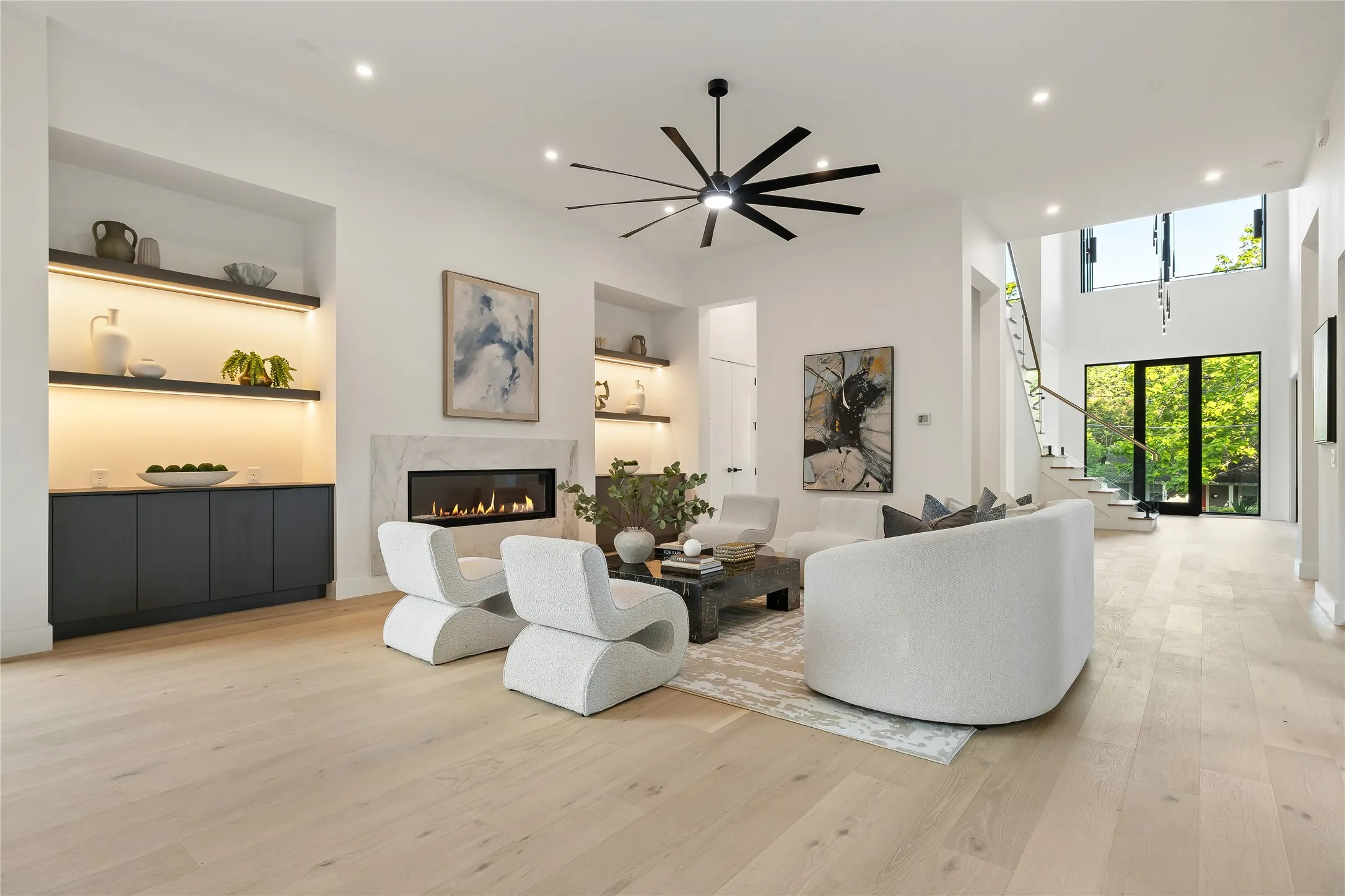 Spacious living area featuring light wood-finish flooring, a contemporary fireplace with a stone surround, and built-in shelving with integrated lighting