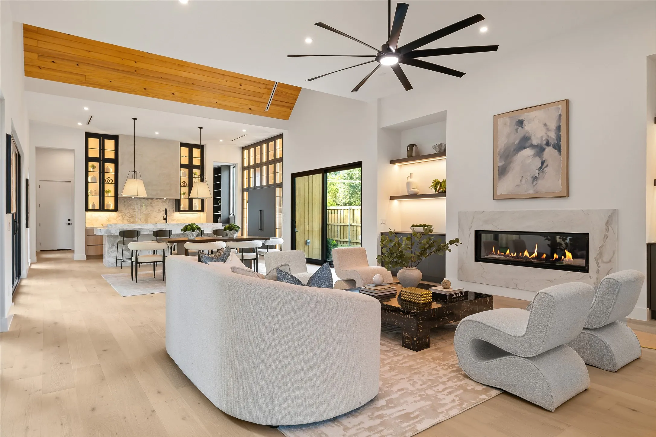 Spacious living area featuring light wood-finish flooring, a contemporary fireplace with a stone surround, and recessed lighting