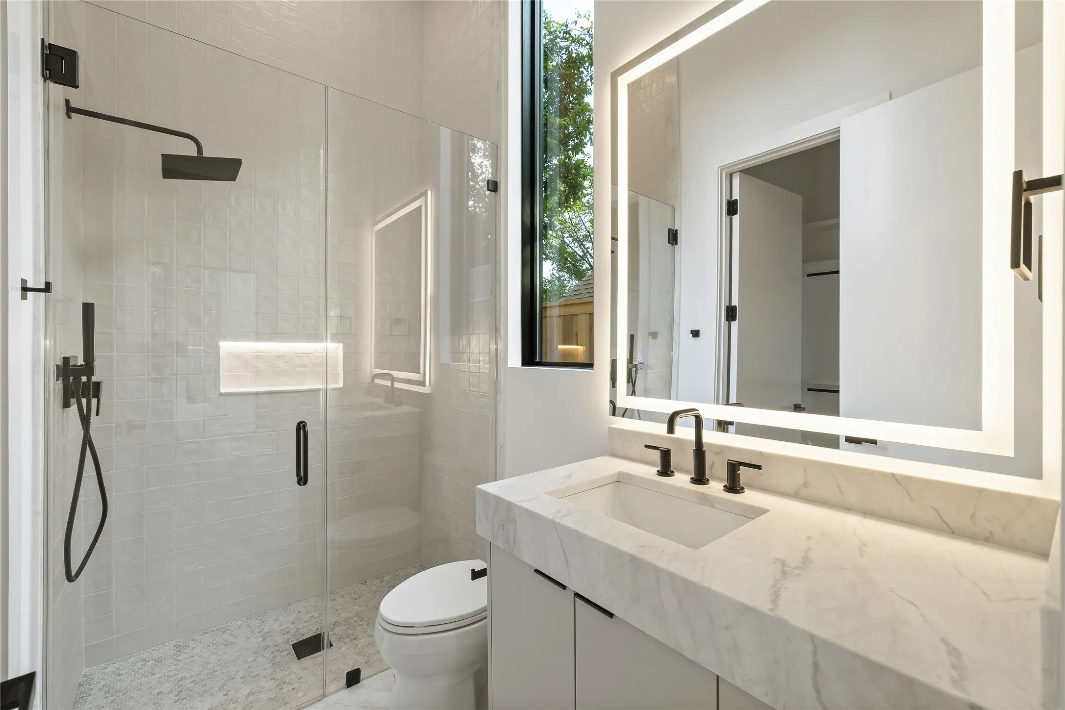 Modern bathroom featuring a frameless glass shower enclosure with matte black fixtures, a built-in shower niche, and a rain shower head