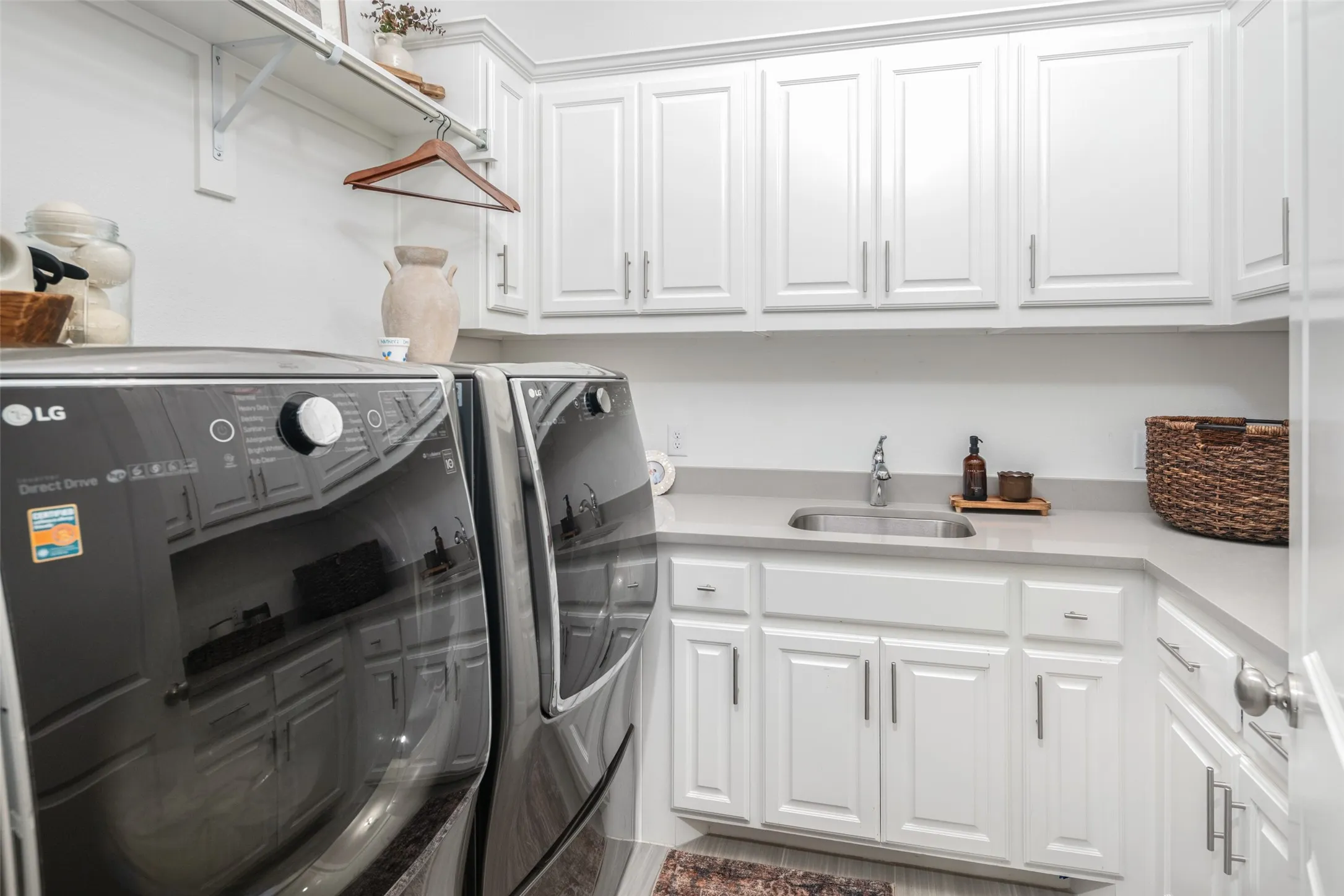 The oversized utility room is thoughtfully designed with abundant upper and lower cabinetry, expansive quartz countertops for folding and organization, a convenient utility sink, and a dedicated hanging area for air-drying garments. Combining exceptional storage with everyday functionality, this well-appointed space makes laundry both efficient and effortless.