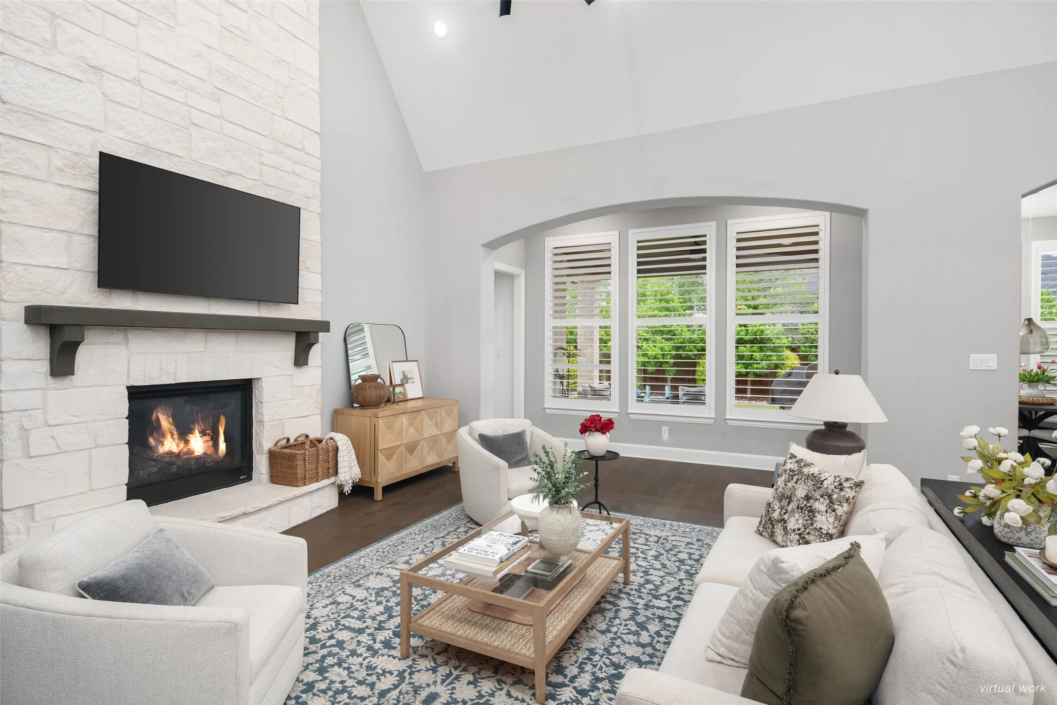 A soaring vaulted ceiling and a wall of oversized windows with plantation shutters flood the space with natural light, enhancing the open-concept design and creating an inviting setting for everyday living and effortless entertaining.