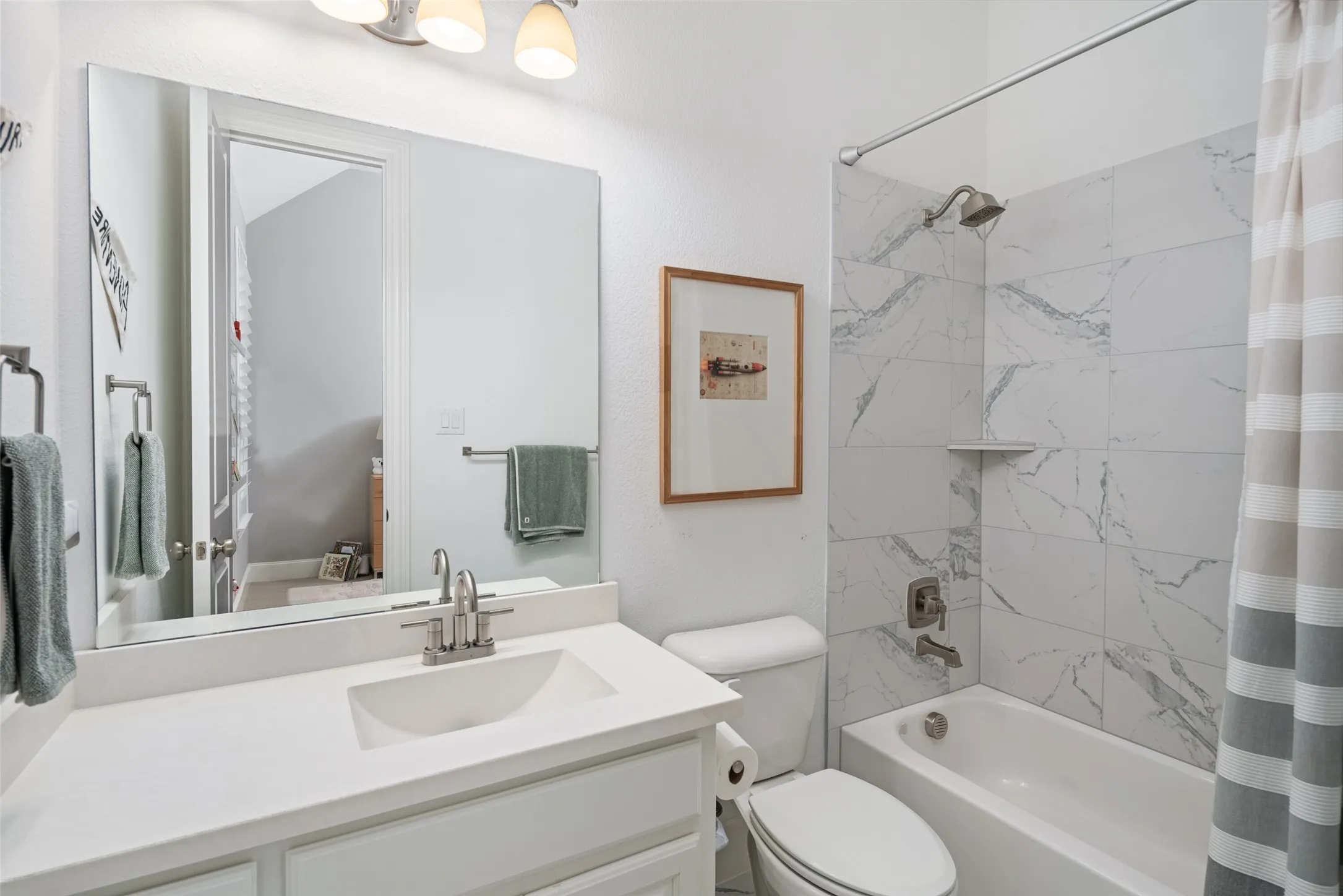 This well-appointed ensuite bathroom features a spacious vanity with generous quartz counter space and storage, along with a shower/tub combination enhanced by elegant floor-to-ceiling designer tile surrounds.