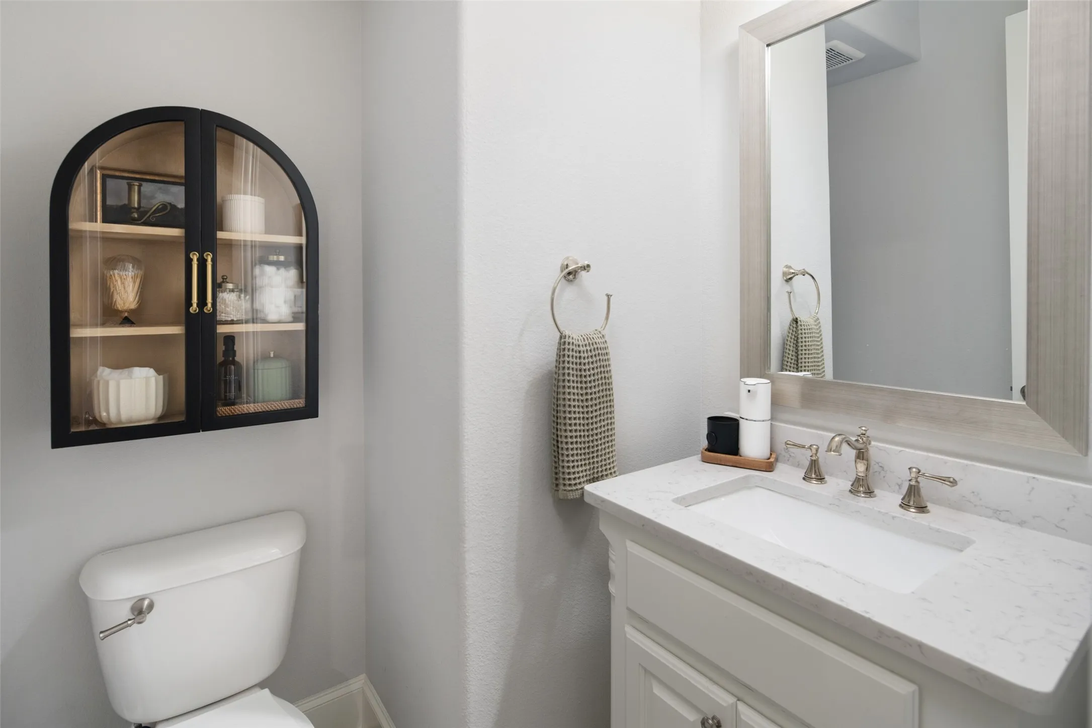 This elegantly appointed powder bath showcases a beautiful custom vanity with a quartz countertop, an undermount sink, an oversized framed mirror, and designer fixtures. Thoughtfully finished with timeless materials and upscale details, it offers guests a sophisticated blend of luxury and style.