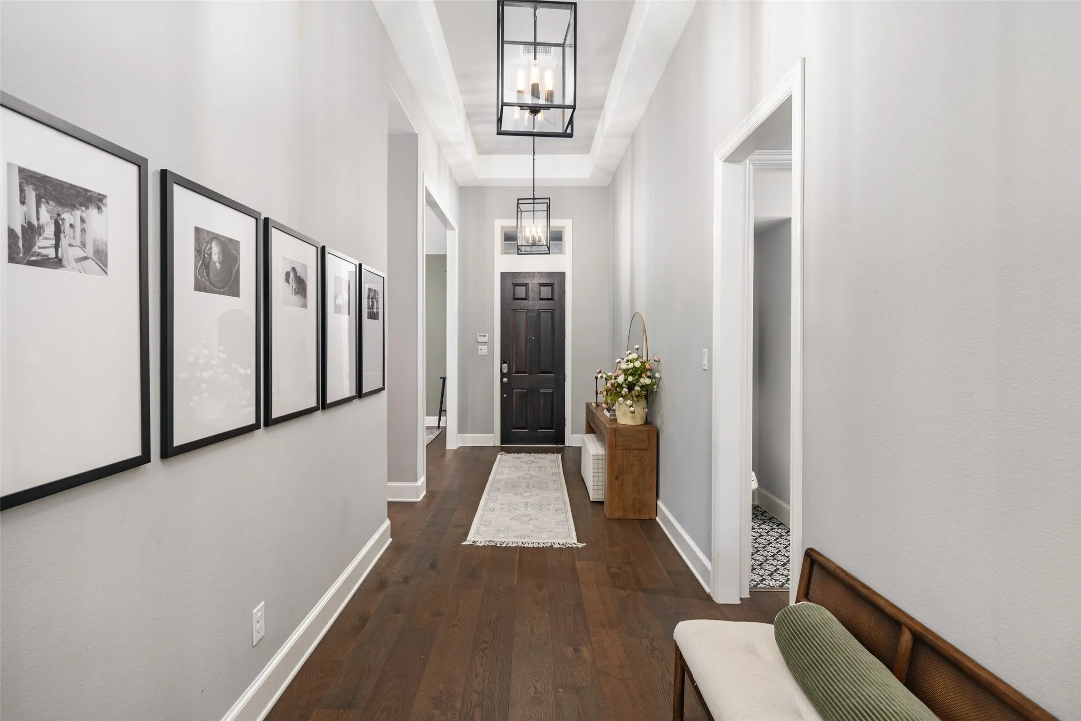 Step inside to a grand entryway featuring an elegant tray ceiling, designer statement lighting, and rich wide plank wood floors that seamlessly flow throughout the main living spaces, creating a warm and sophisticated first impression.