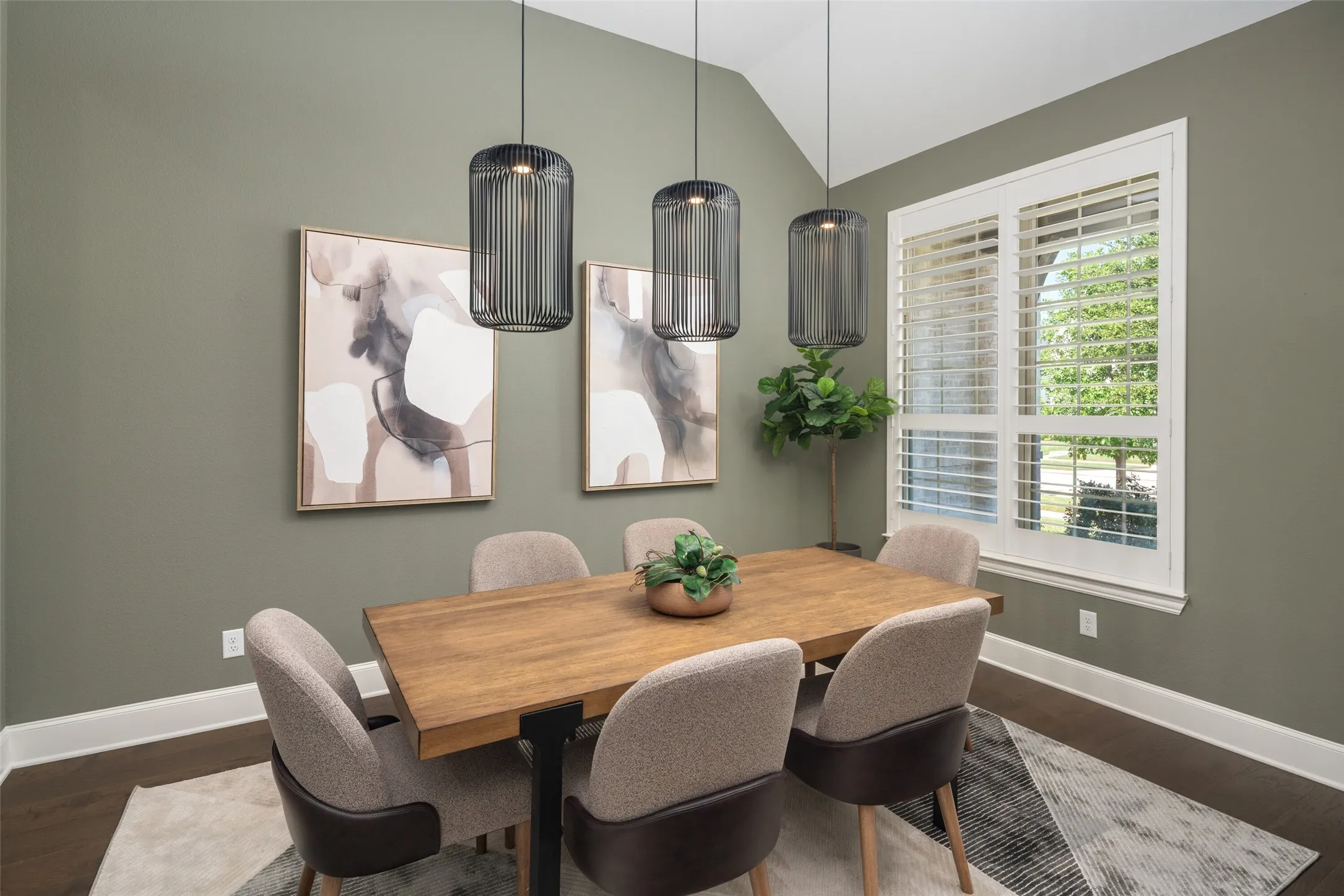 A refined dining room designed to impress, featuring soaring ceilings, custom designer lighting, an elegant accent wall, and plantation shutters that frame beautiful natural light.
