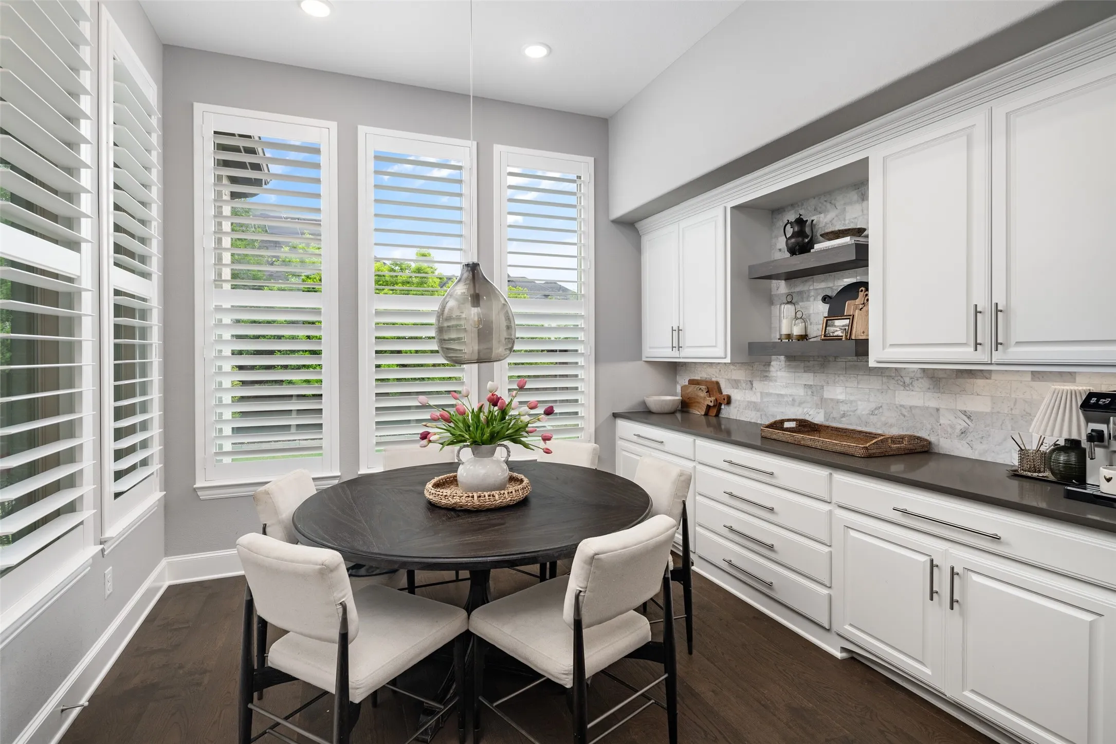 The sun-filled breakfast nook is surrounded by large windows with plantation shutters, creating a bright and inviting space to start the day.