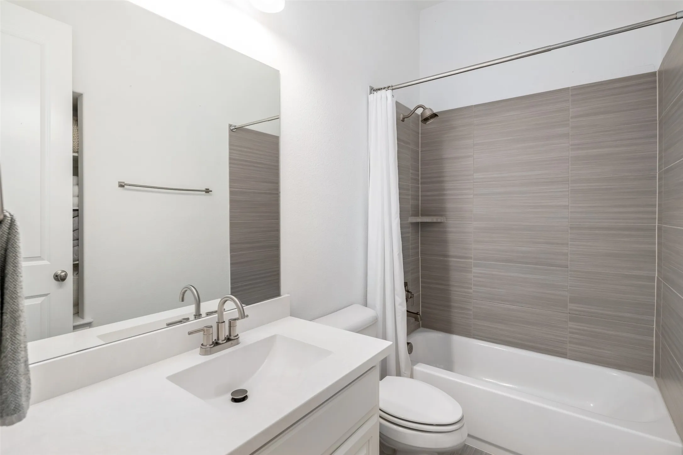 This private ensuite bathroom is thoughtfully designed with an oversized vanity offering generous counter space and storage, complemented by a shower/tub combination with elegant floor-to-ceiling designer tile surrounds. Blending timeless finishes with everyday functionality, this well-appointed bath provides comfort and convenience for family members or guests.
