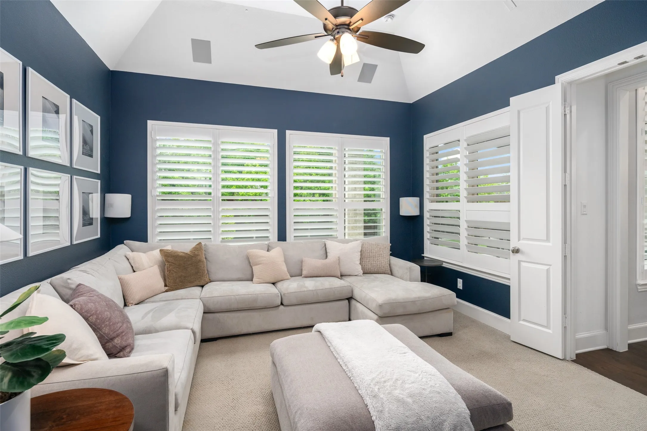 The spacious media room offers the perfect retreat for movie nights and game days, featuring a soaring vaulted ceiling, plush carpeting, a ceiling fan, and built-in surround sound speakers. Large windows with plantation shutters fill the room with natural light while creating a comfortable, flexible space for entertainment, relaxation, or family gatherings.