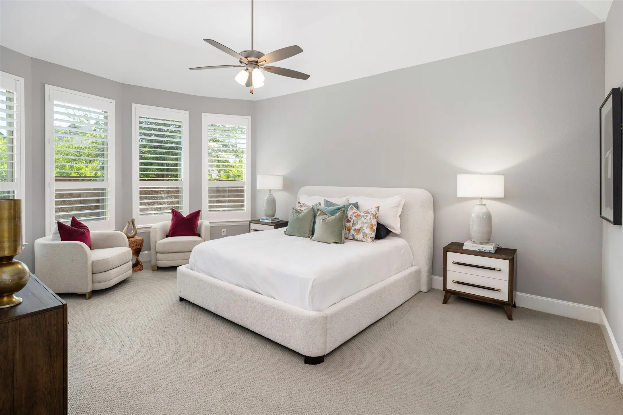 Retreat to the luxurious oversized primary suite featuring a soaring vaulted ceiling, an elegant window bump-out, and a wall of windows adorned with plantation shutters that fill the room with abundant natural light. Plush carpeting enhances the serene atmosphere, creating a spacious and sophisticated retreat designed for ultimate comfort and relaxation.