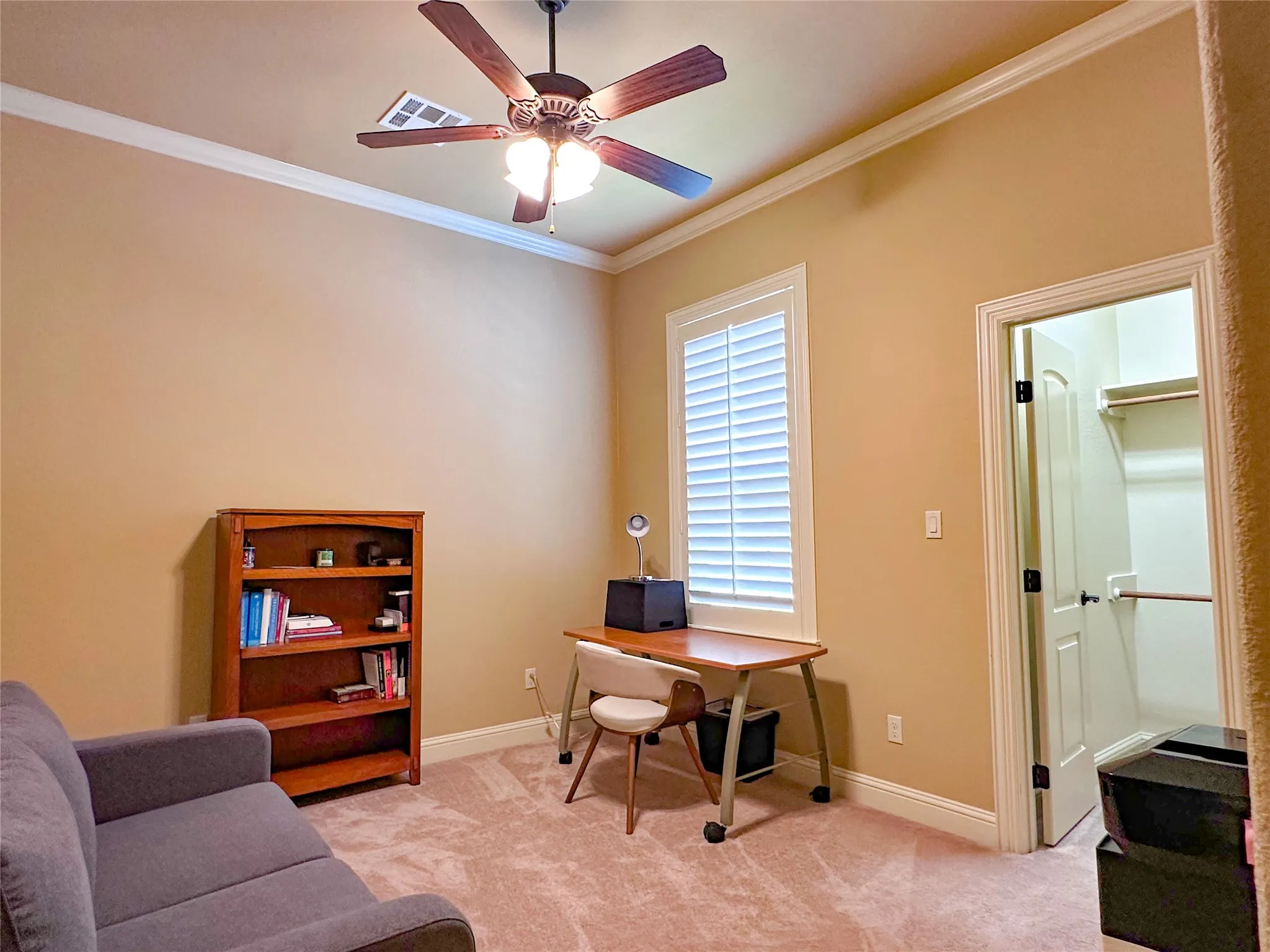 Spacious room with high ceilings and crown molding, featuring a ceiling fan, plush carpeting, and a window with plantation shutters