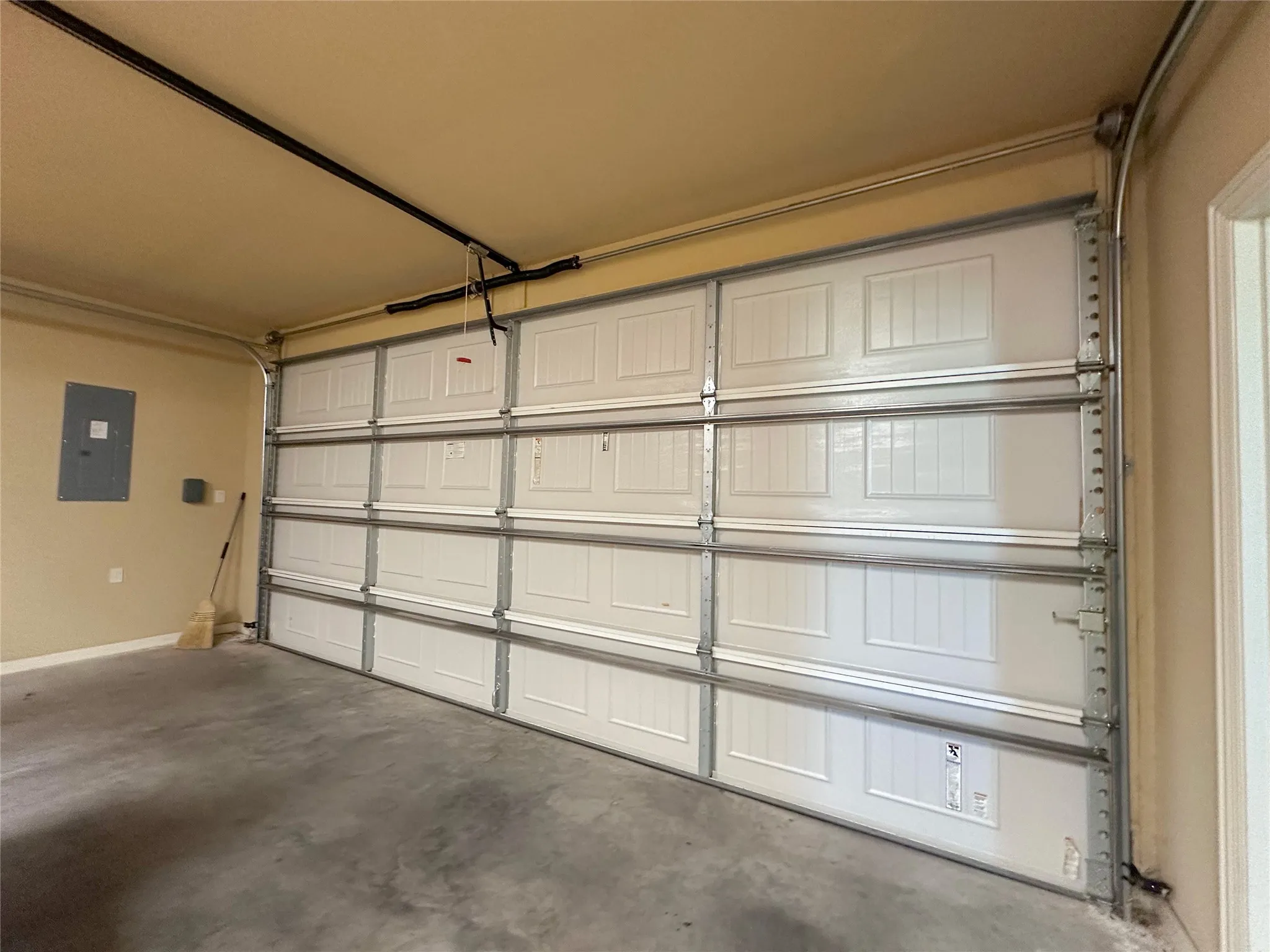 Spacious garage featuring a white paneled door, exposed metal track system, and concrete flooring
