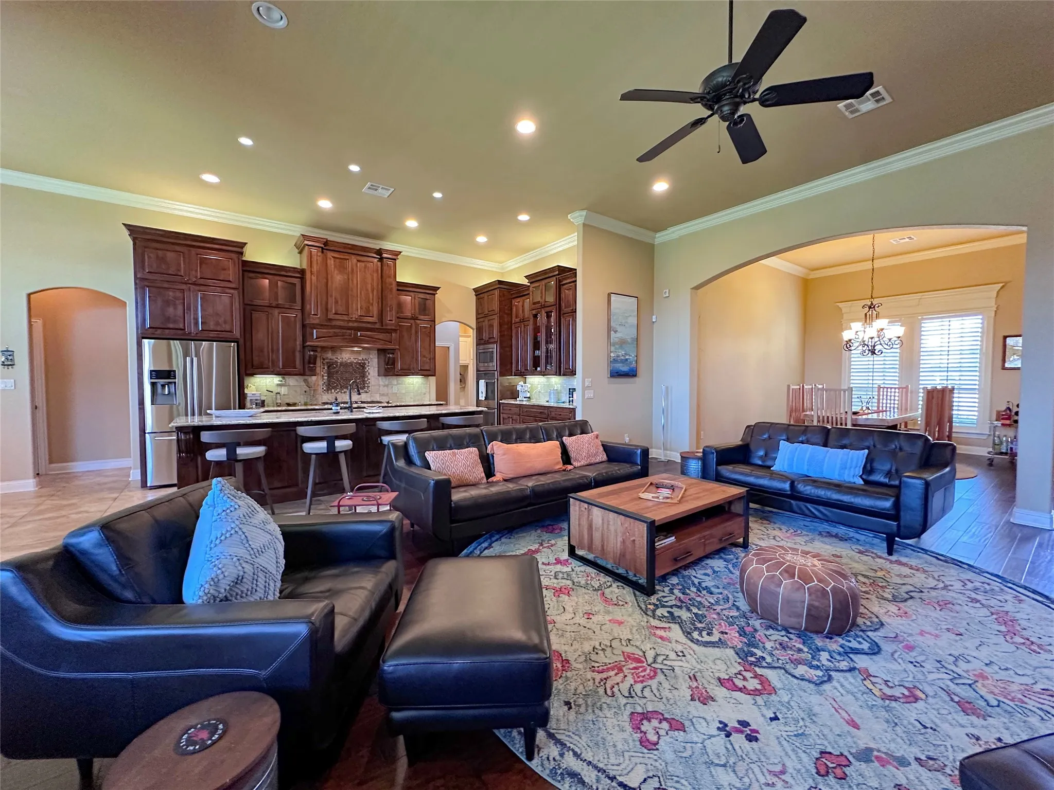 Open-concept living area featuring wood-finish flooring, a ceiling fan, recessed lighting, and crown molding