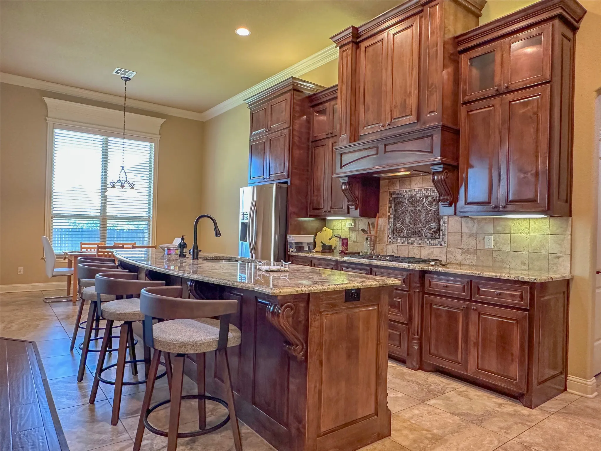 Kitchen featuring rich wood cabinetry, granite countertops, stainless steel appliances, and a tile backsplash with decorative inset