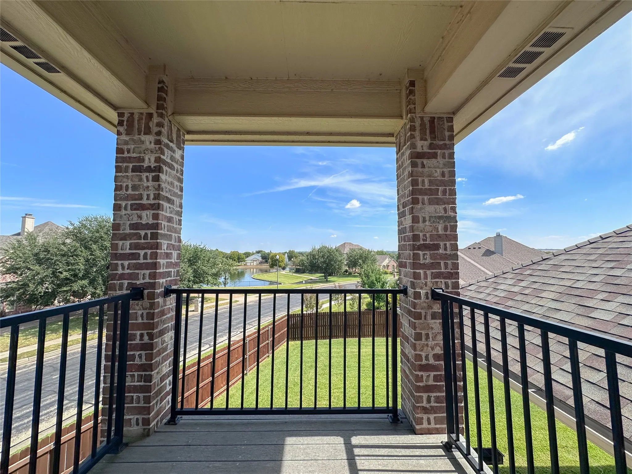 Second-story balcony featuring brick columns, black metal railing, and composite decking