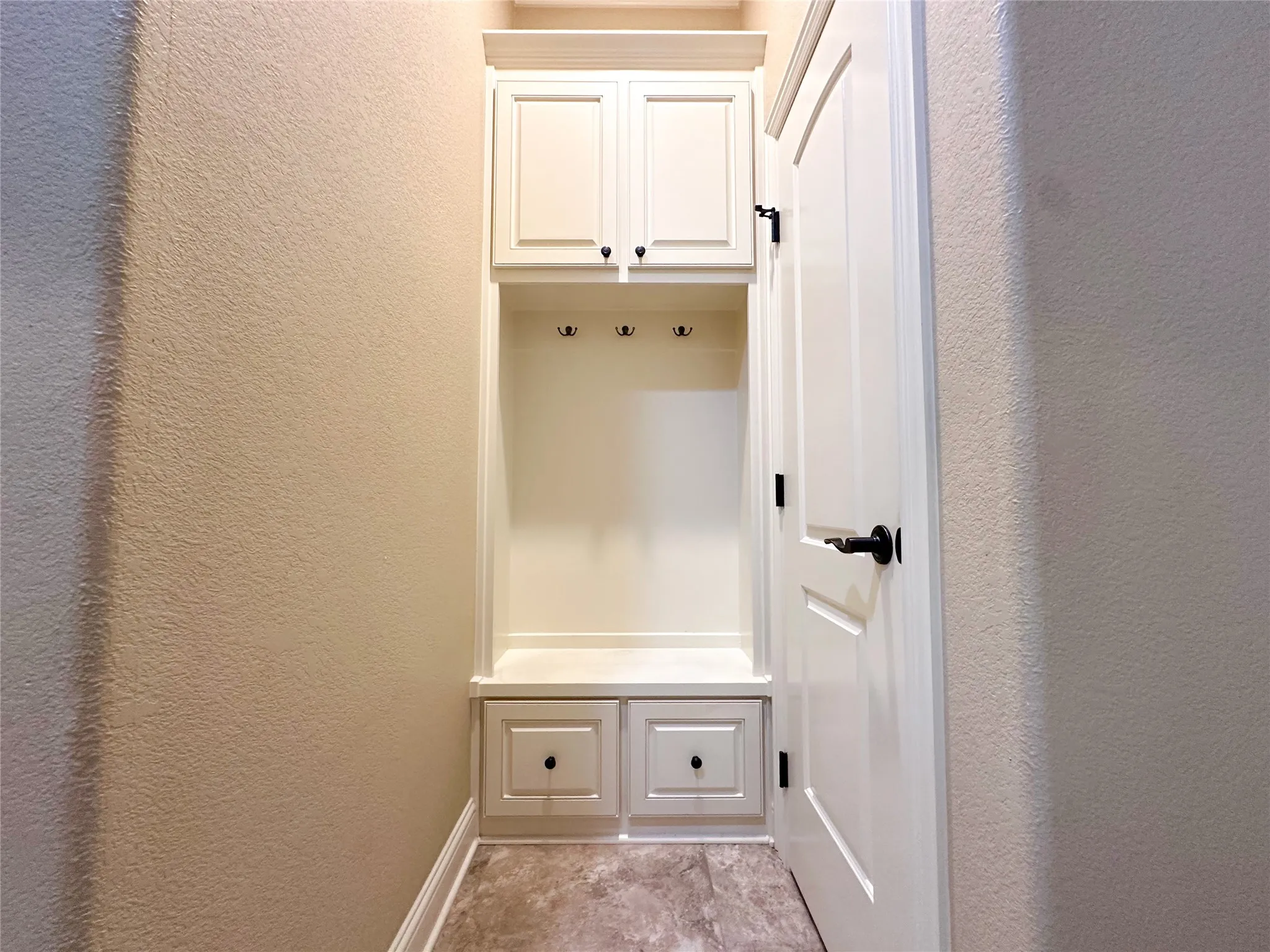 Built-in mudroom station featuring upper cabinetry, storage bench, three coat hooks, and two lower drawers
