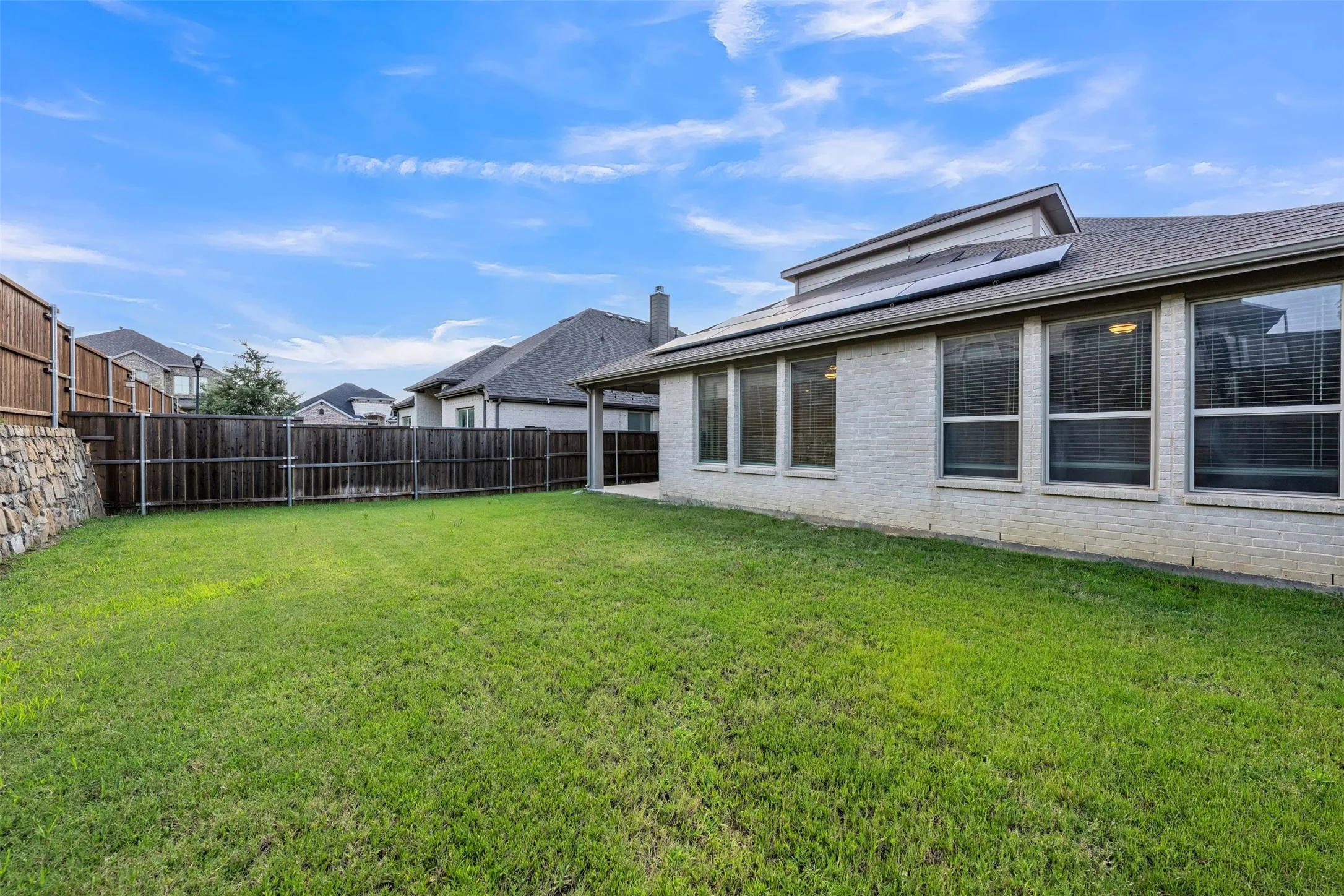 Backyard at 5149 Cantle Ct in Fort Worth, Texas, Tarrant County, is large and flat with rock retaining wall and wooden privacy fence.