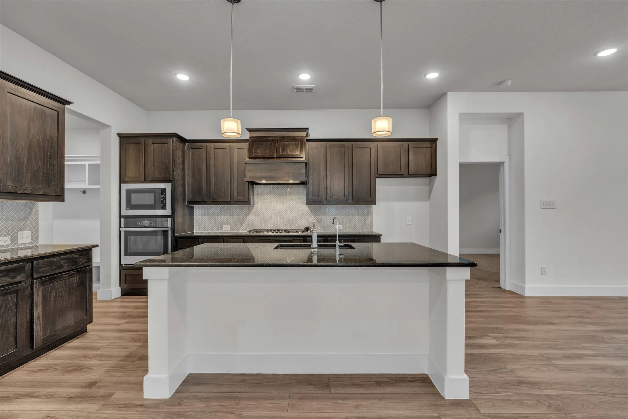 Kitchen at 5149 Cantle Ct in Fort Worth, Texas, Tarrant County, with large kitchen island, brown wooden cabinets, neutral herringbone backsplash, and separate cooktop.