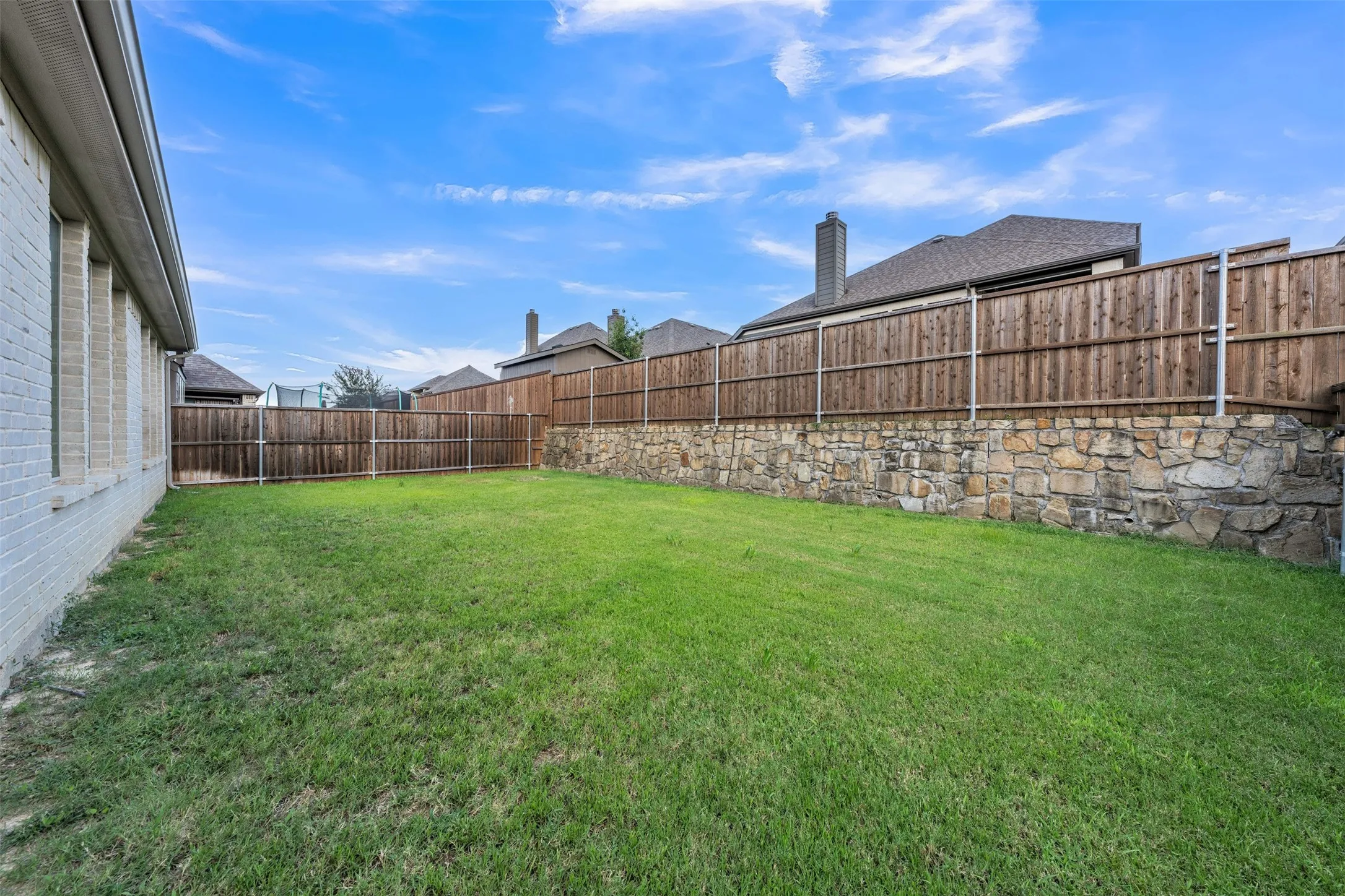 Backyard at 5149 Cantle Ct in Fort Worth, Texas, Tarrant County, is large and flat with rock retaining wall and wooden privacy fence.
